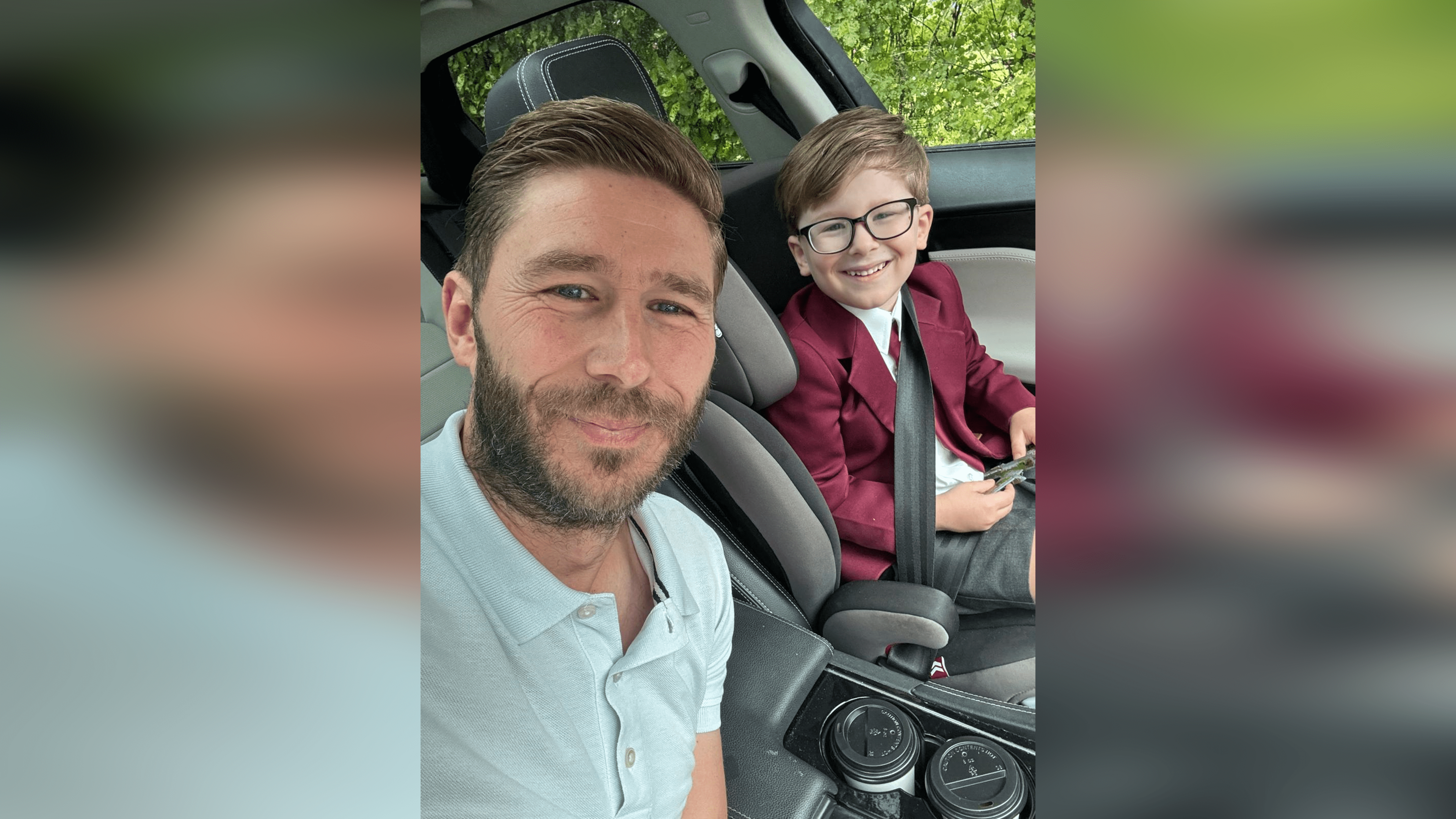 Stacey, who has brown hair and a beard, and his son Paddy are sat in the car on the way to school. Stacey has a pale blue polo shirt on while Paddy is wearing a school uniform.
