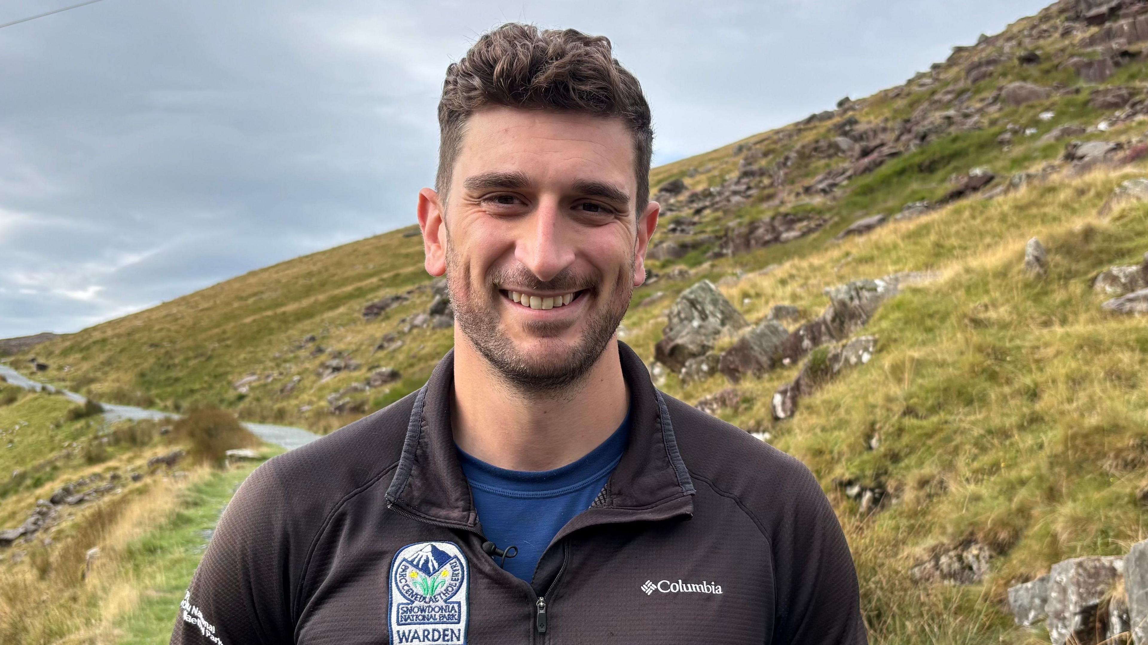 Alun Jones of Eryri National Park Authority smiling at the camera, standing on one of the paths up Yr Wyddfa