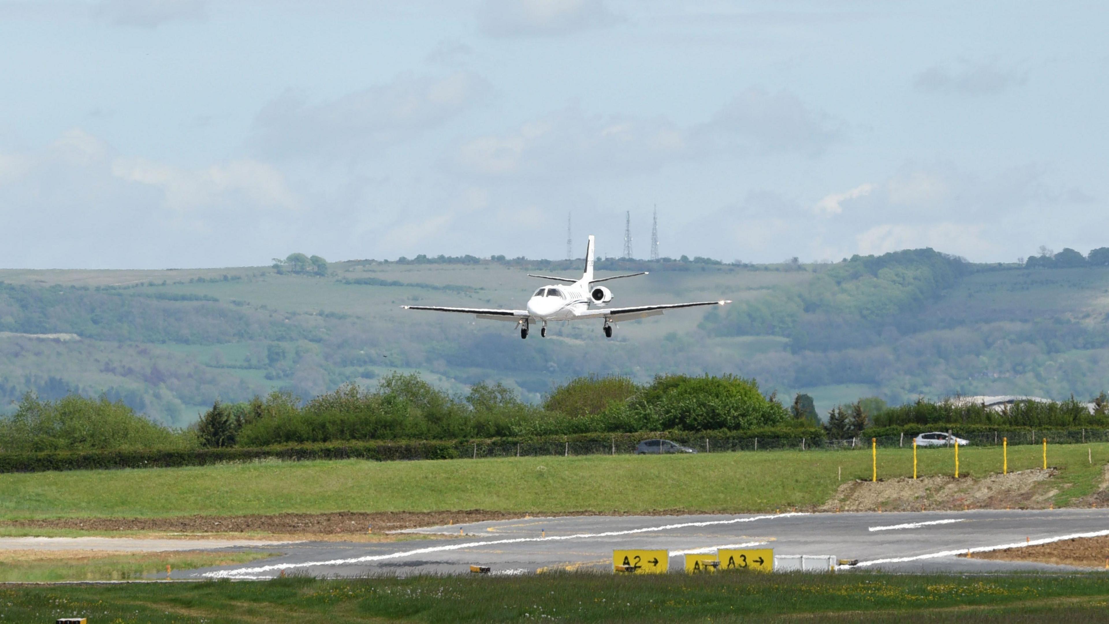 A small white plane coming in to land on the runway at Gloucestershire Airport.