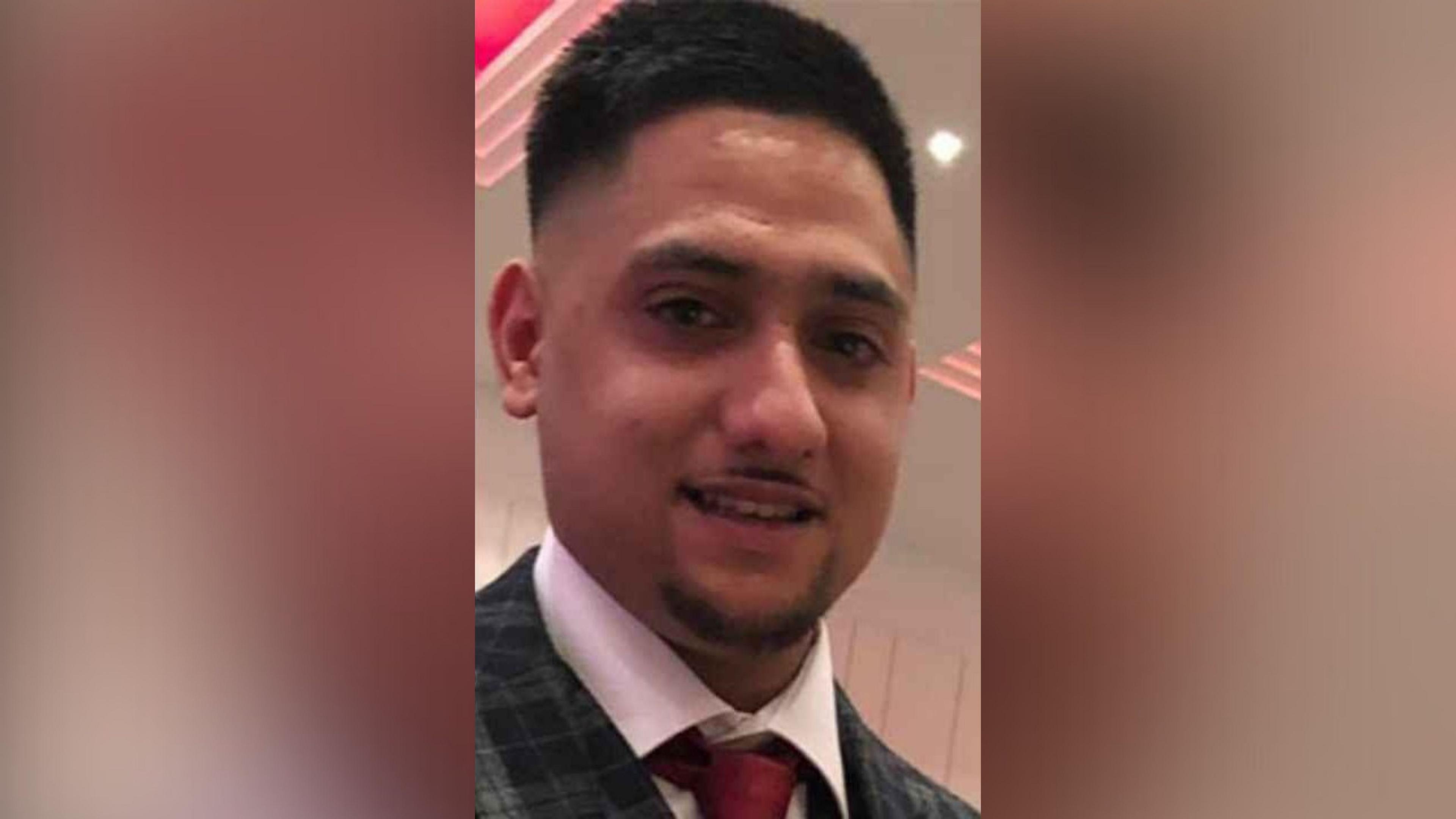 A photo of Mohammed Duraab Khan. The picture shows his head and neck - he is wearing a white shirt, red tie and black and green checked jacket