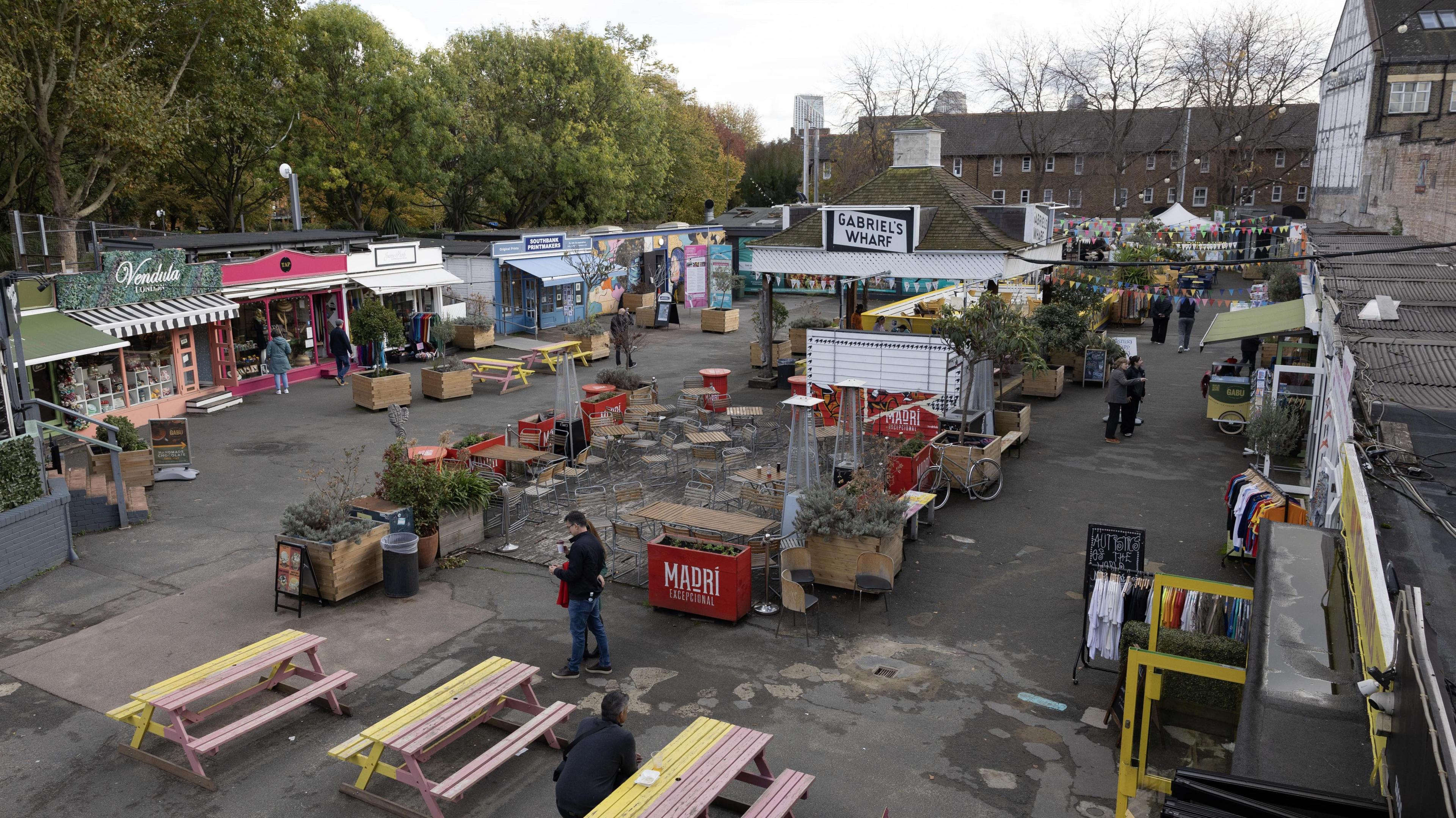 An elevated view of Gabriel's Wharf showing small shops around the edge of the site. In the middle, there are benches and potted trees.