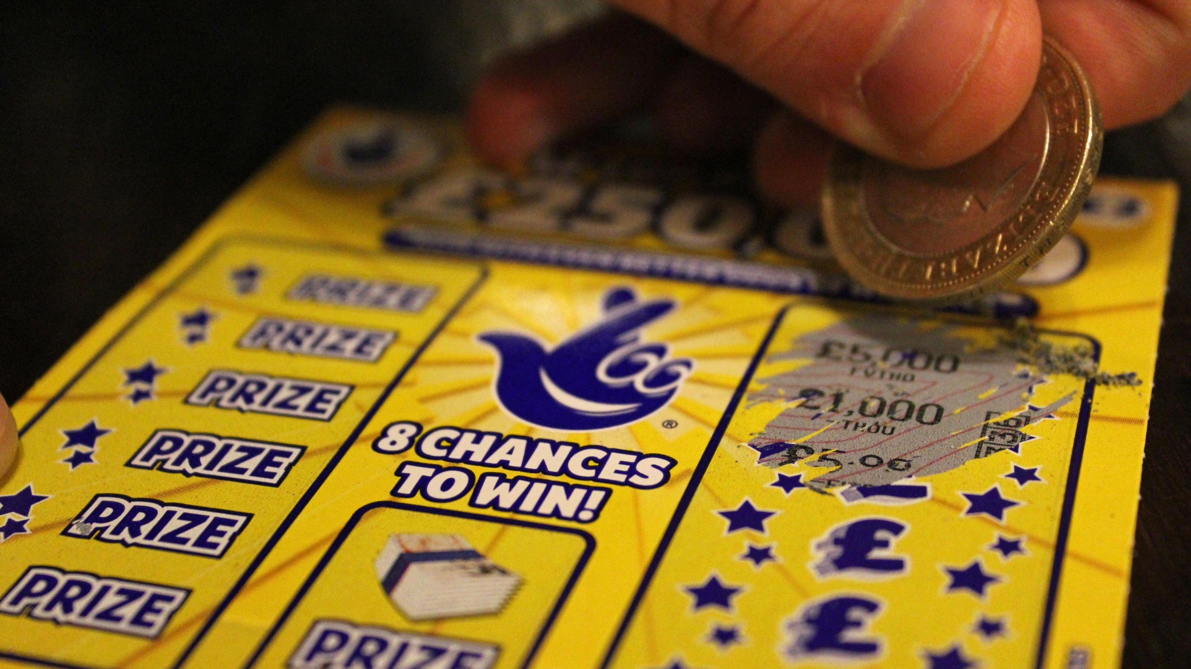 A yellow Lotto scratch card with the pound signs, the word prize and the crossed fingers logo in a dark blue. The wording '8 chances to win' is centred, in white capital letters. 