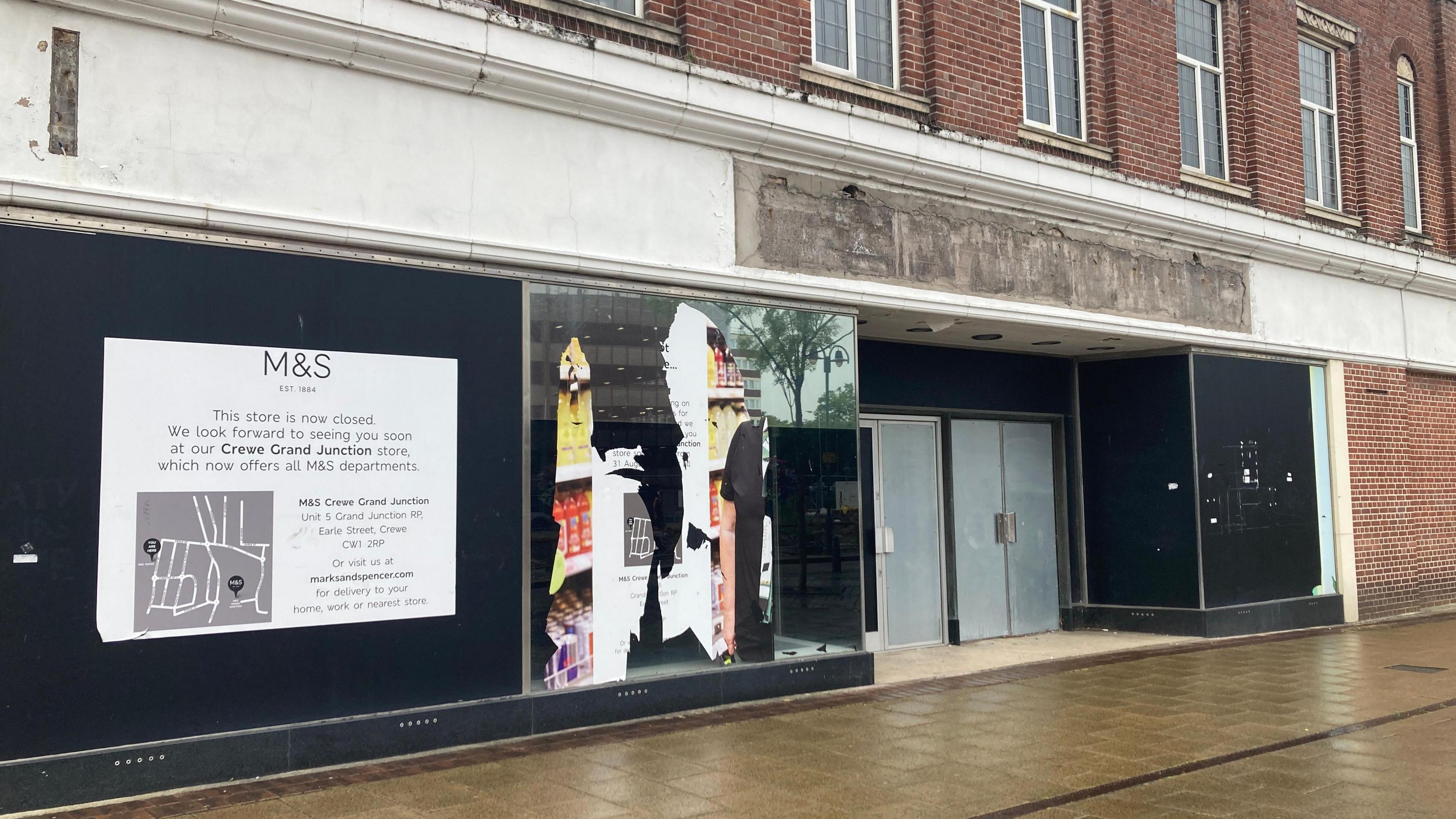 A brick-built, two-storey building with blacked-out windows and doors. There are posters and damage to some parts of the black cladding.