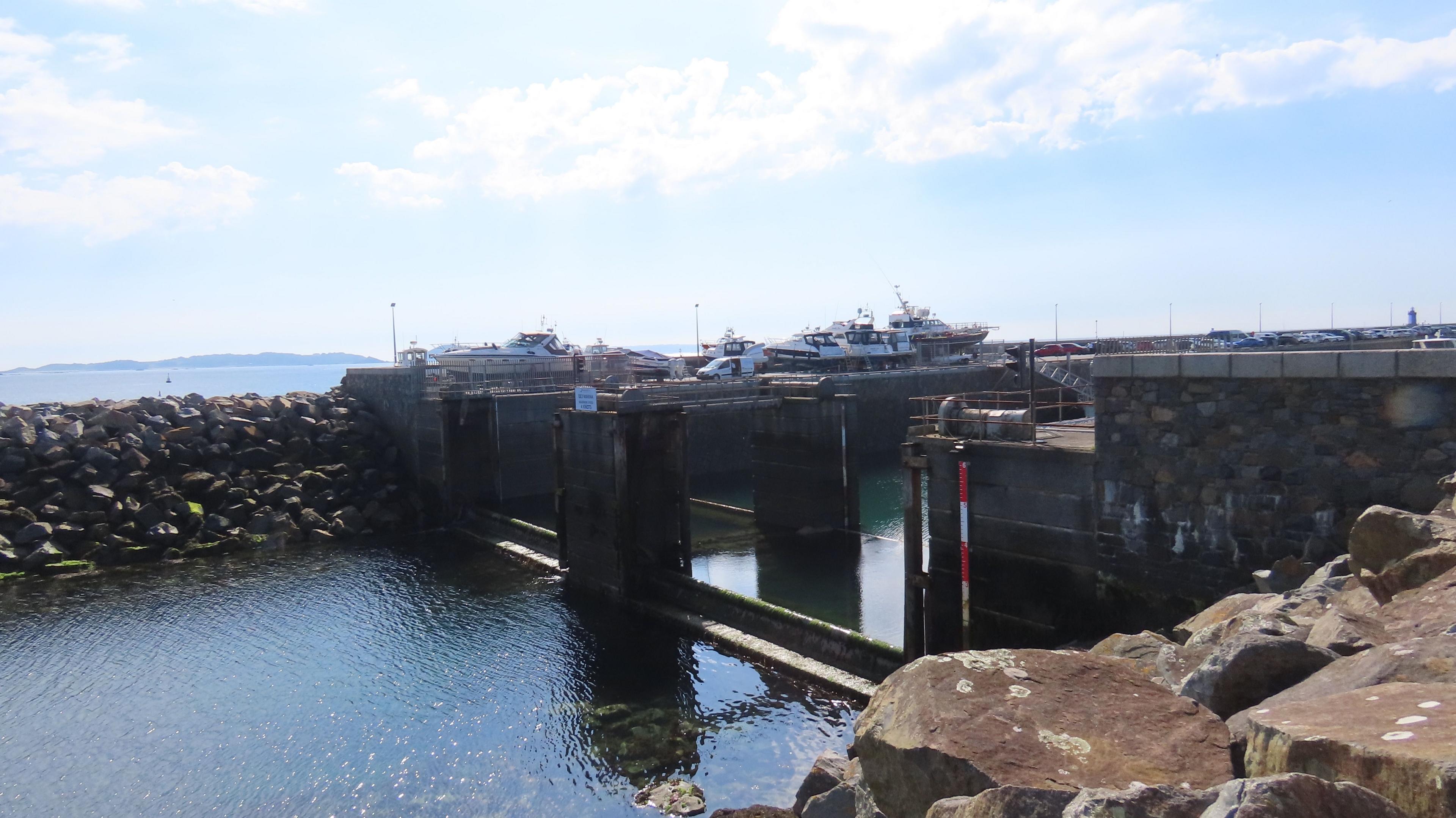 The QEII Marina's gates. Water is low and there is rock armour in the foreground and some boats in the distance.