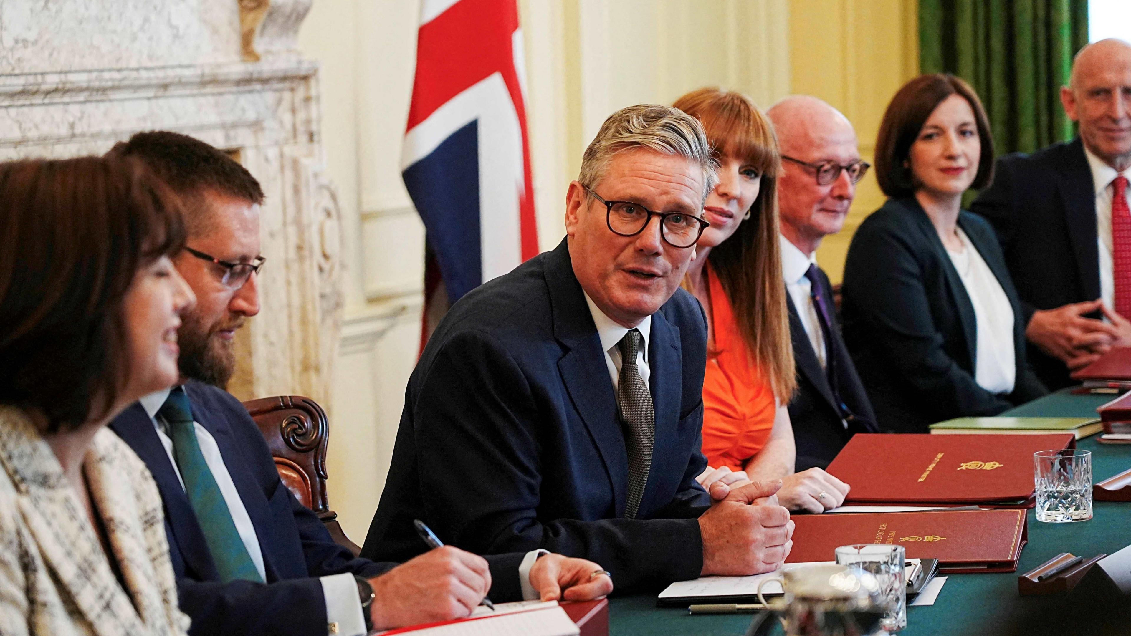 Sir Keir Starmer wearing a suit and tie is talking to his colleagues in the cabinet room in Downing Street 