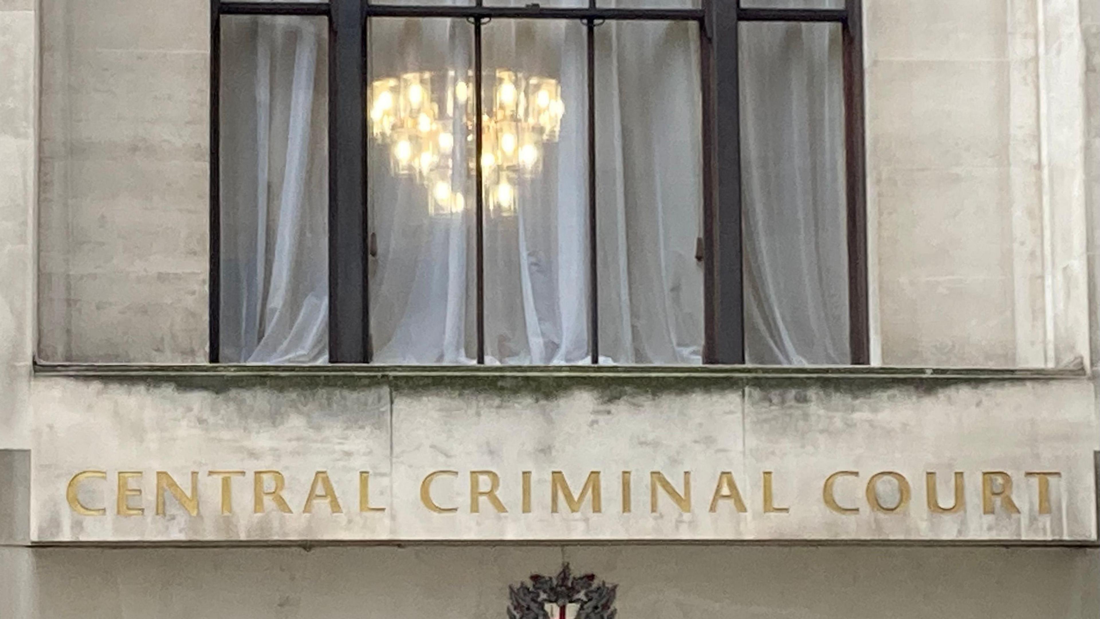 The front of the Old Bailey with the words Central Criminal Court in gold and illuminated lamps showing though the window.