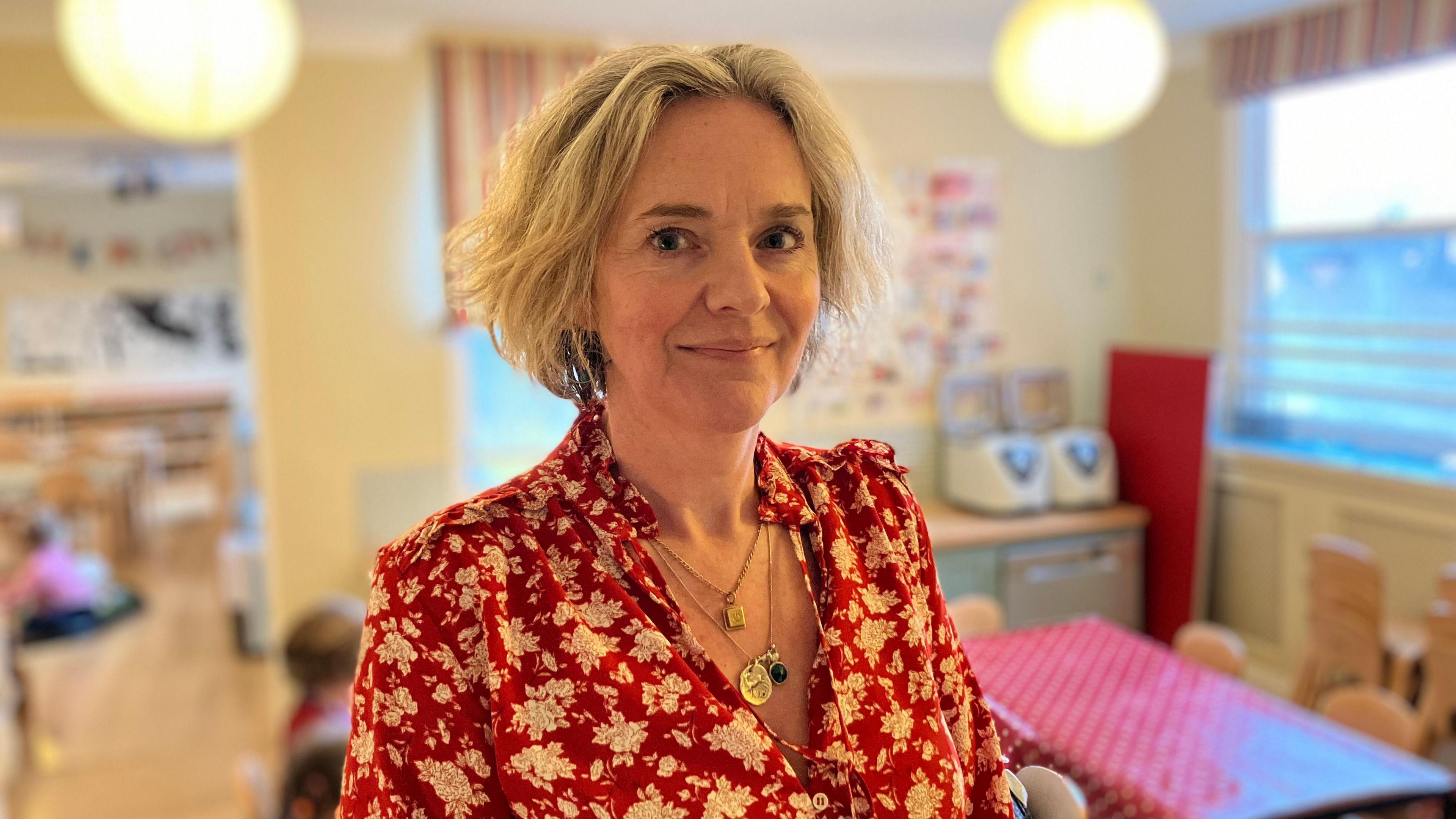 Claire Kenyon smiles looking directly in front of her. She is wearing a white and red blouse. 