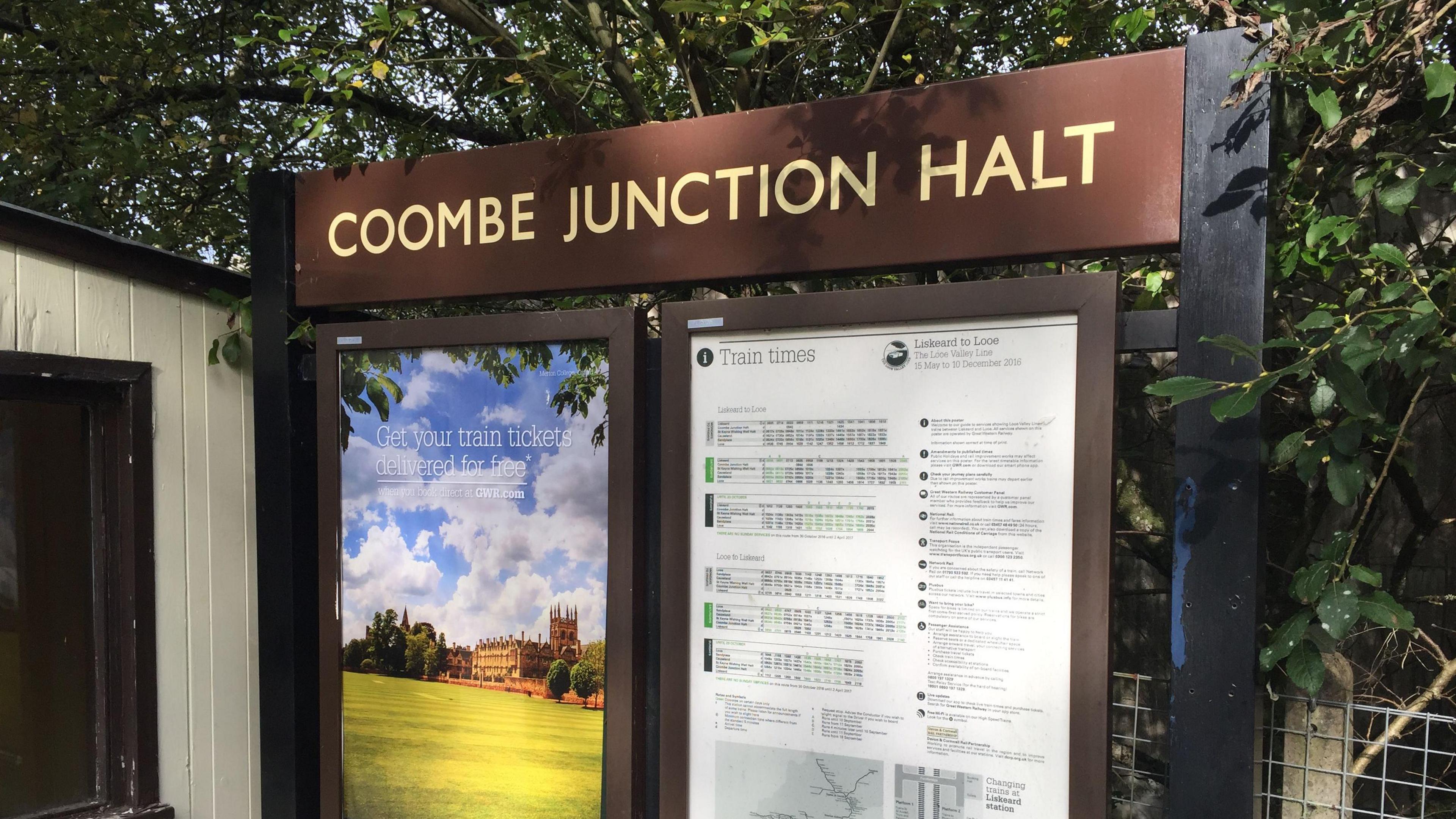 Brown sign with writing saying Coombe Junction Halt in cream coloured writing, and the rail timetable below