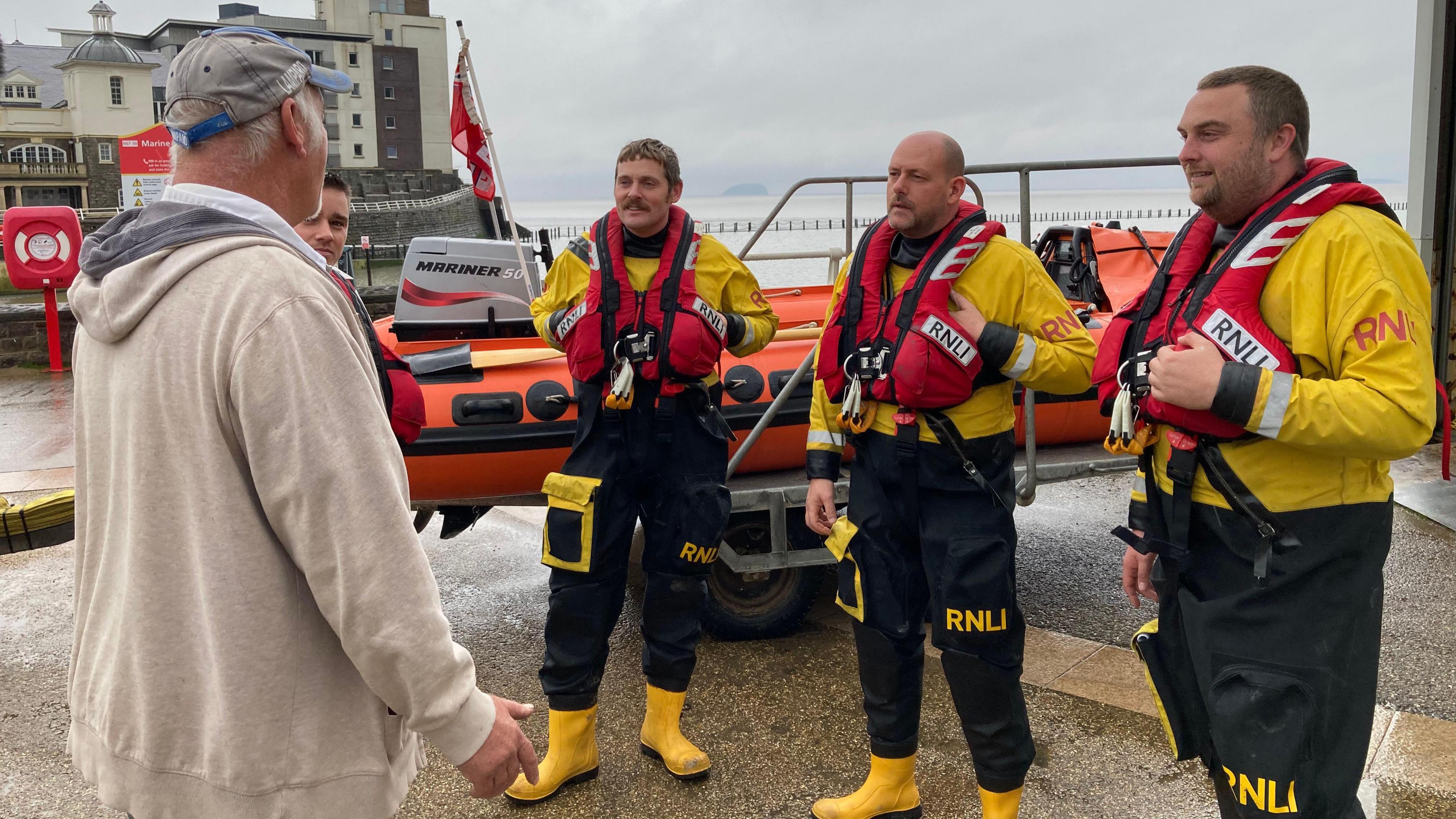 Mr Grant is standing on the left, facing three member of the rescue crew who saved his life. The rescue crew are in uniform and life jackets. They are all looking at Mr Grant.