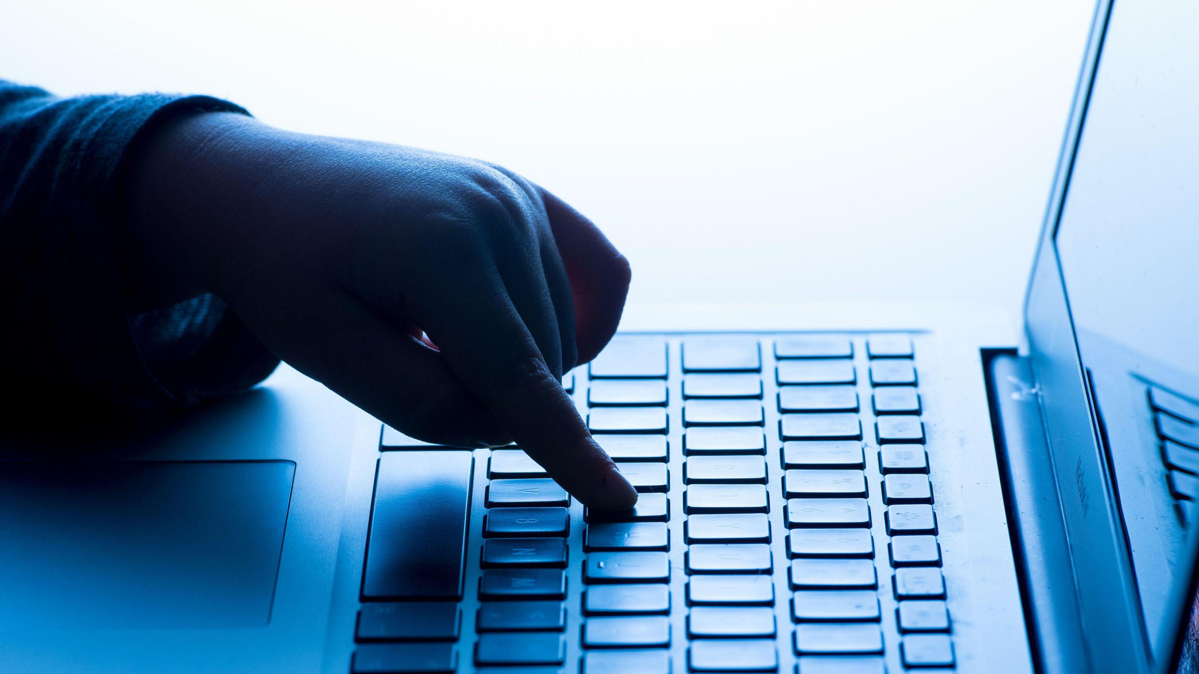 A child's hand pressing a key of a laptop keyboard.