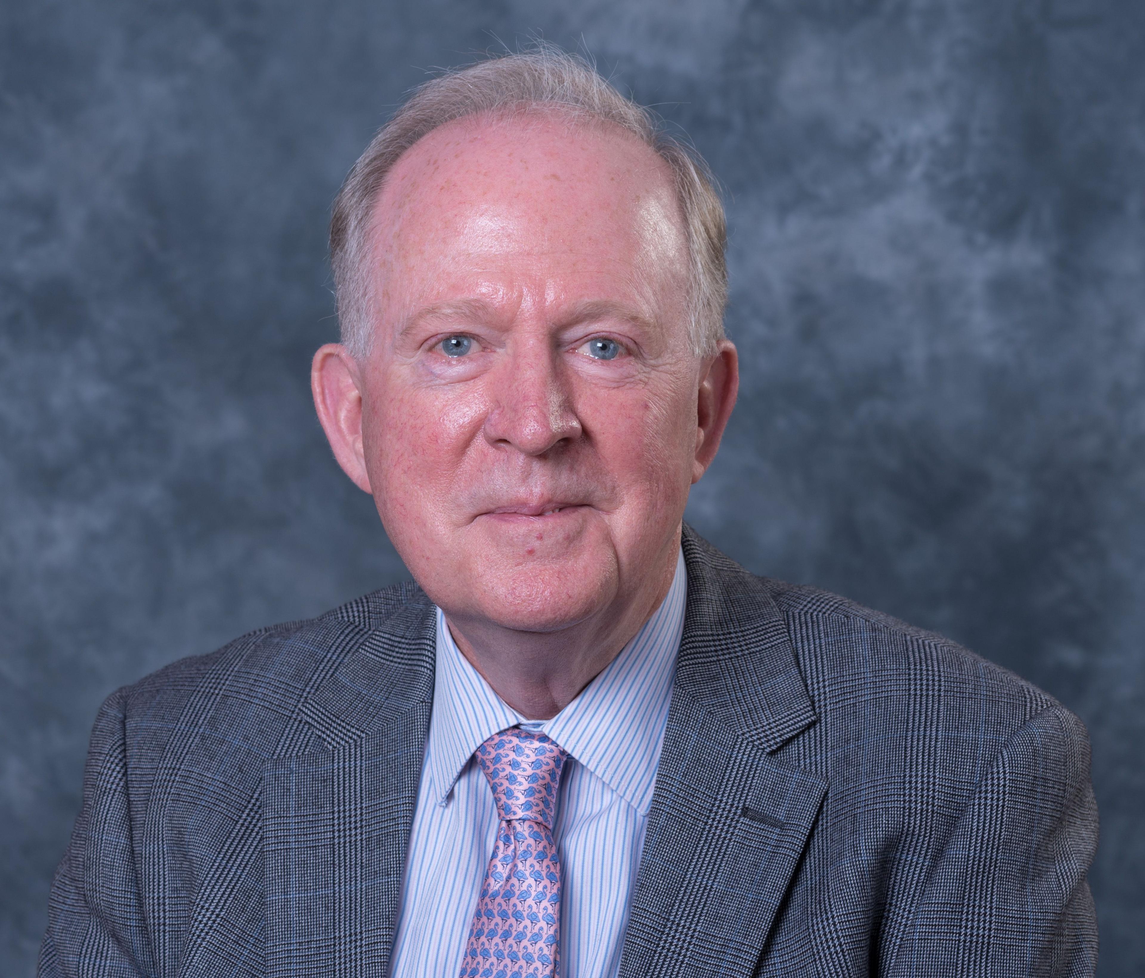 David Chambers wearing a grey suit with a pink and purple tie, looking at the camera against a grey backdrop.