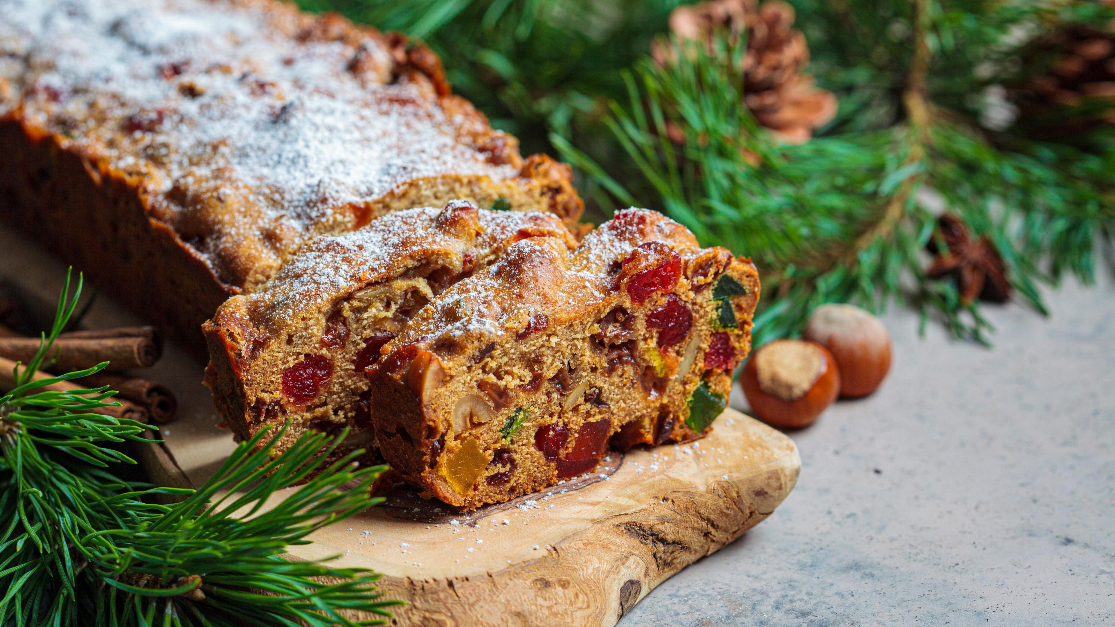 Traditional Christmas fruit cake on a wooden board in a festive decoration, dark background.