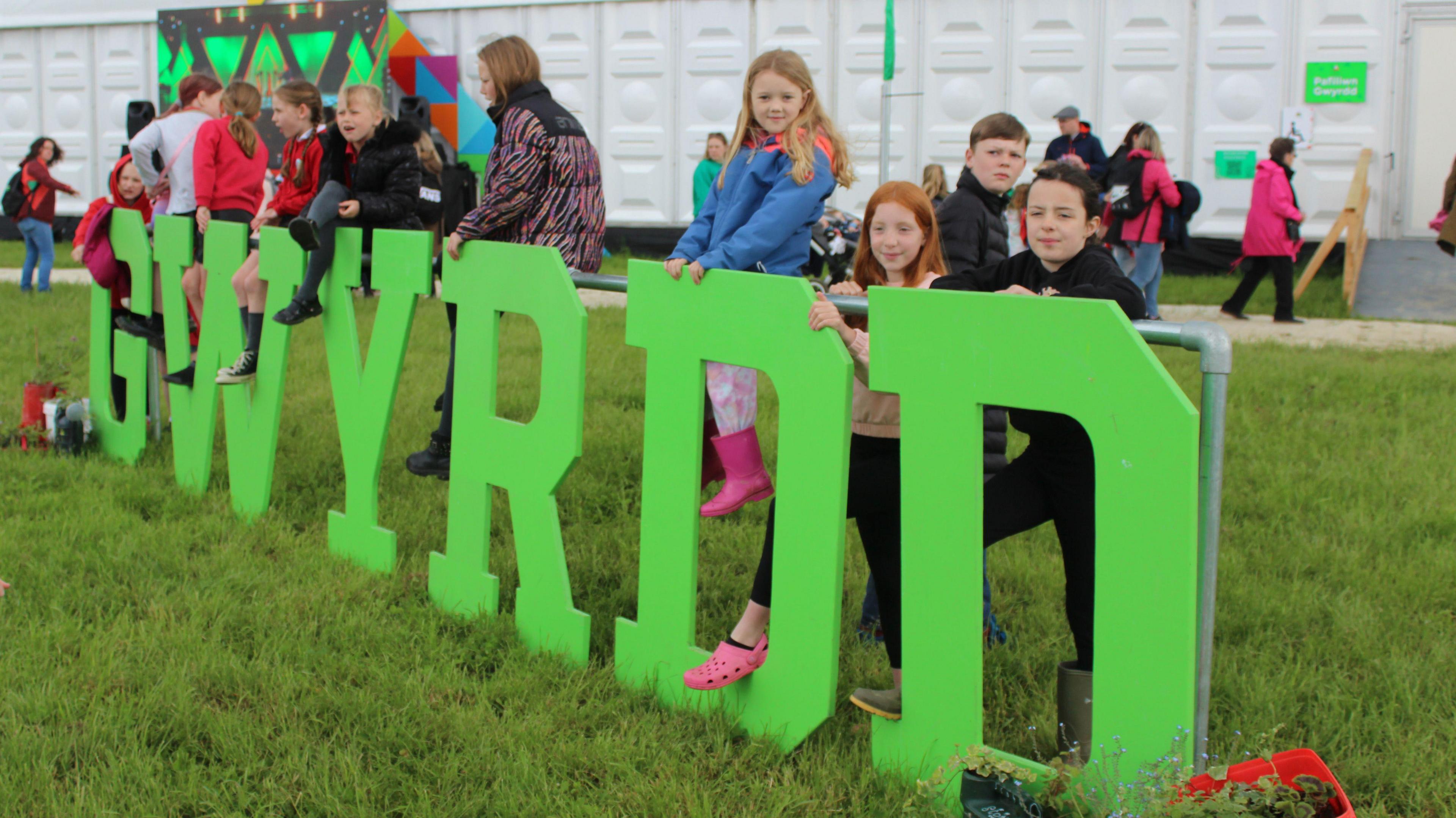 plant yn dringo ar yr arwydd gwyrdd tu allan i'r pafiliwn ar faes yr Eisteddfod