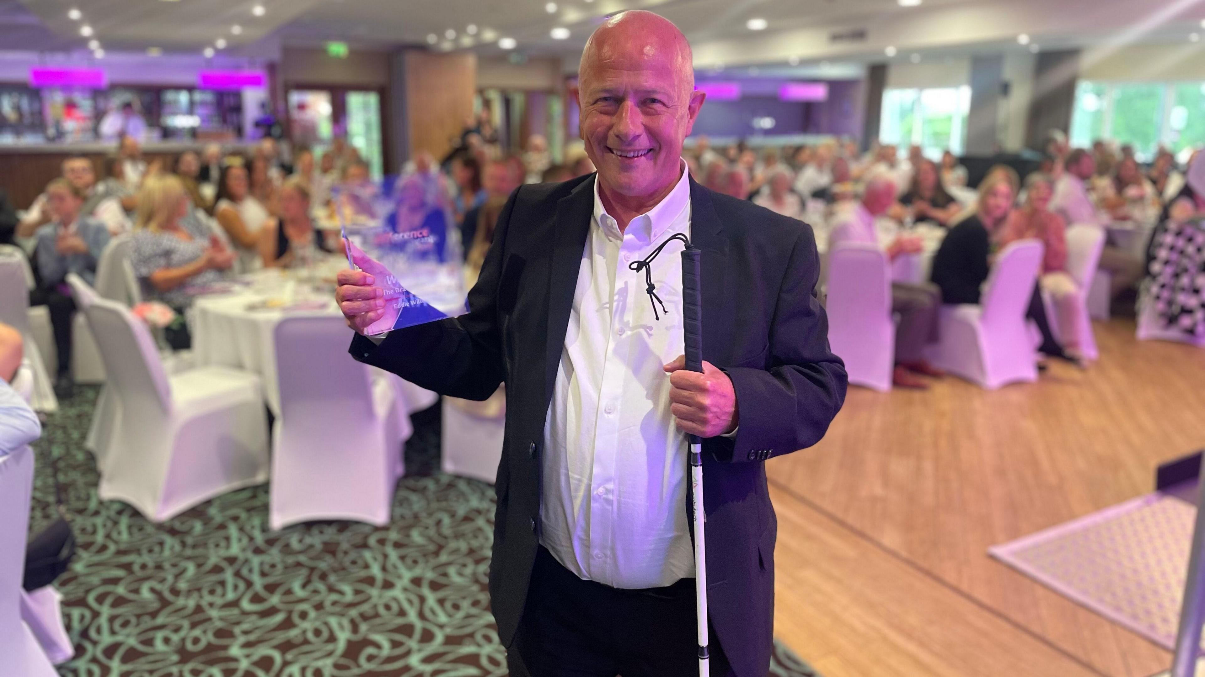 Eddie, who uses a white cane, standing with his bravery award in the awards ceremony.