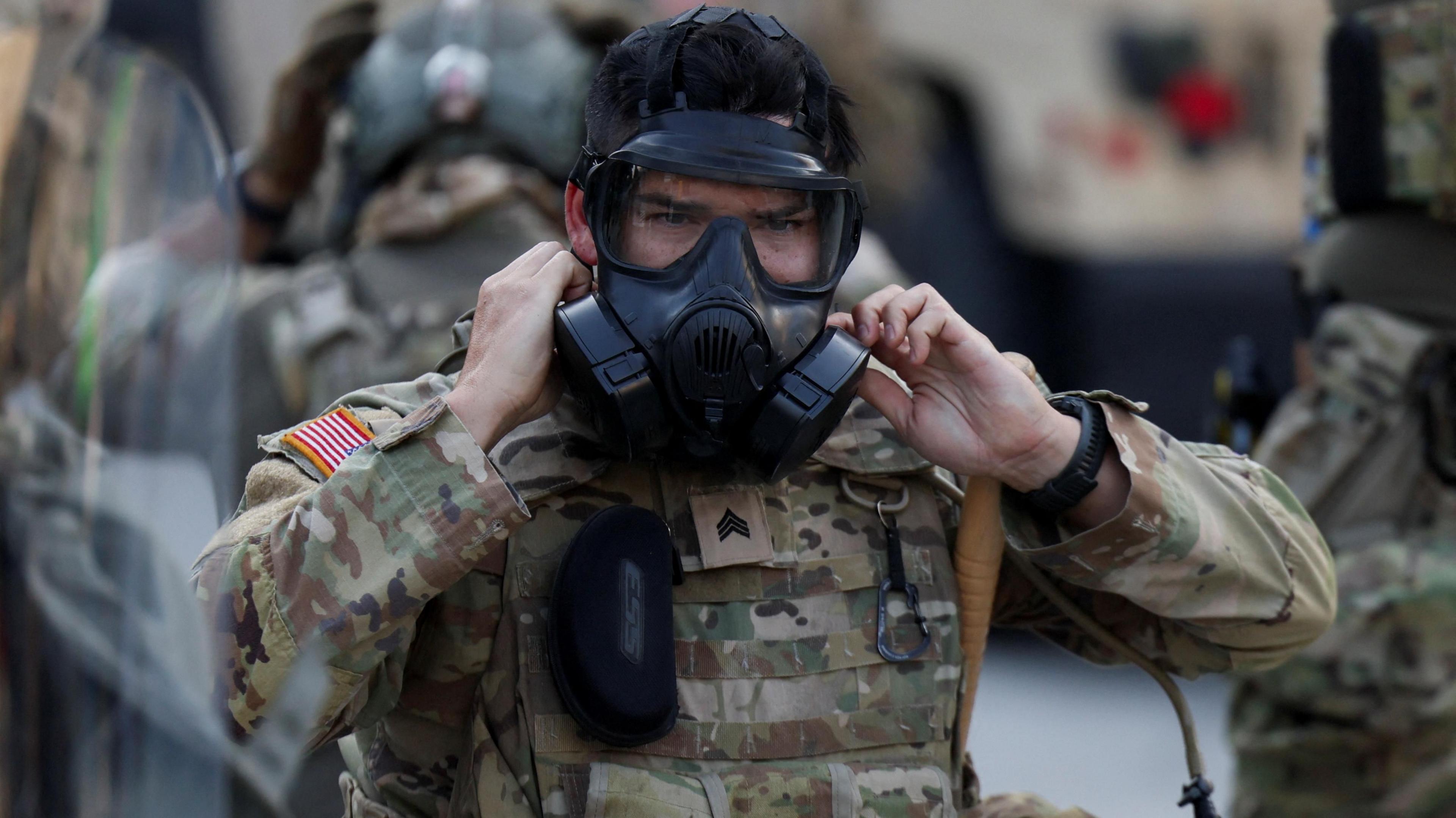 California National Guard member in camouflage colored uniform puts on black gas mask