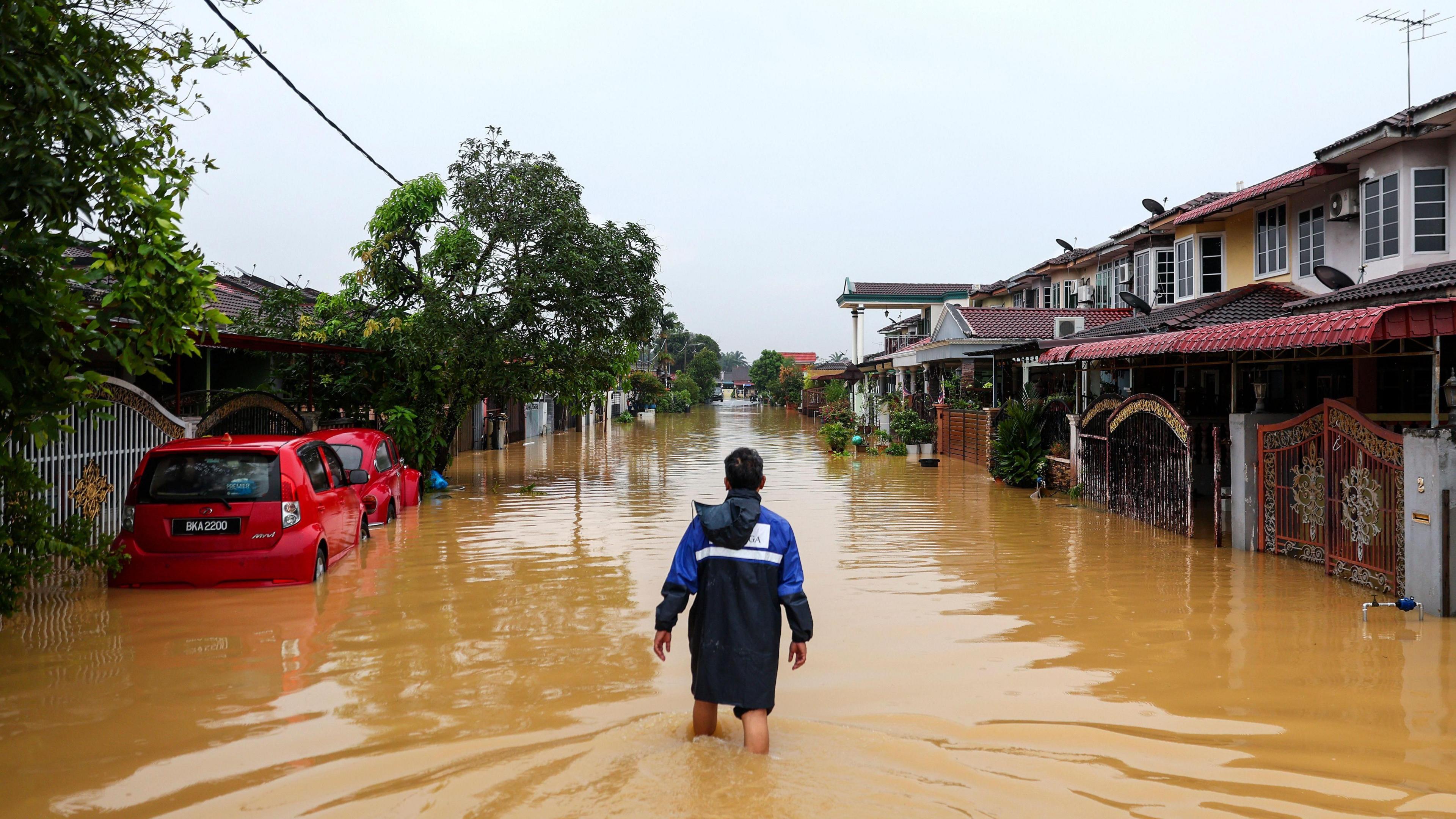 A person standing in the middle of a flooded street, where water is hitting them at knee-level