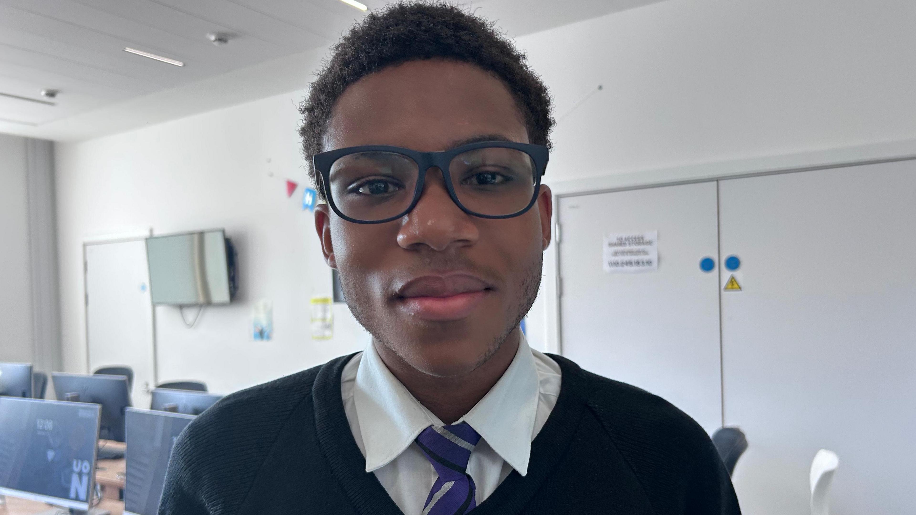 A boy in a school uniform wearing dark-framed glasses.
