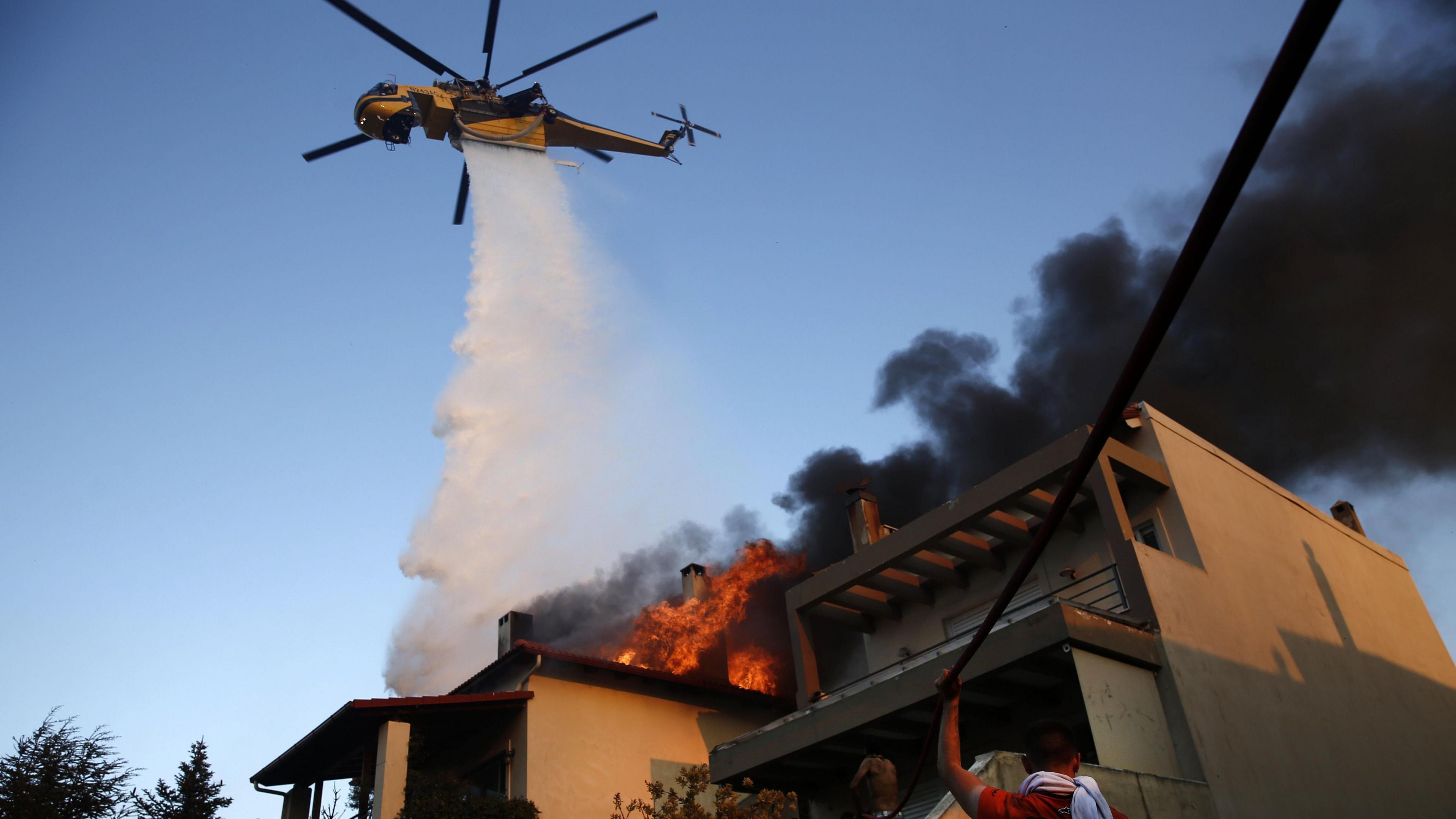 A firefighting helicopter and volunteers battle to put out a fire burning houses in the residential area of Kryoneri, in the suburbs of Athens, Greece, 26 July 202