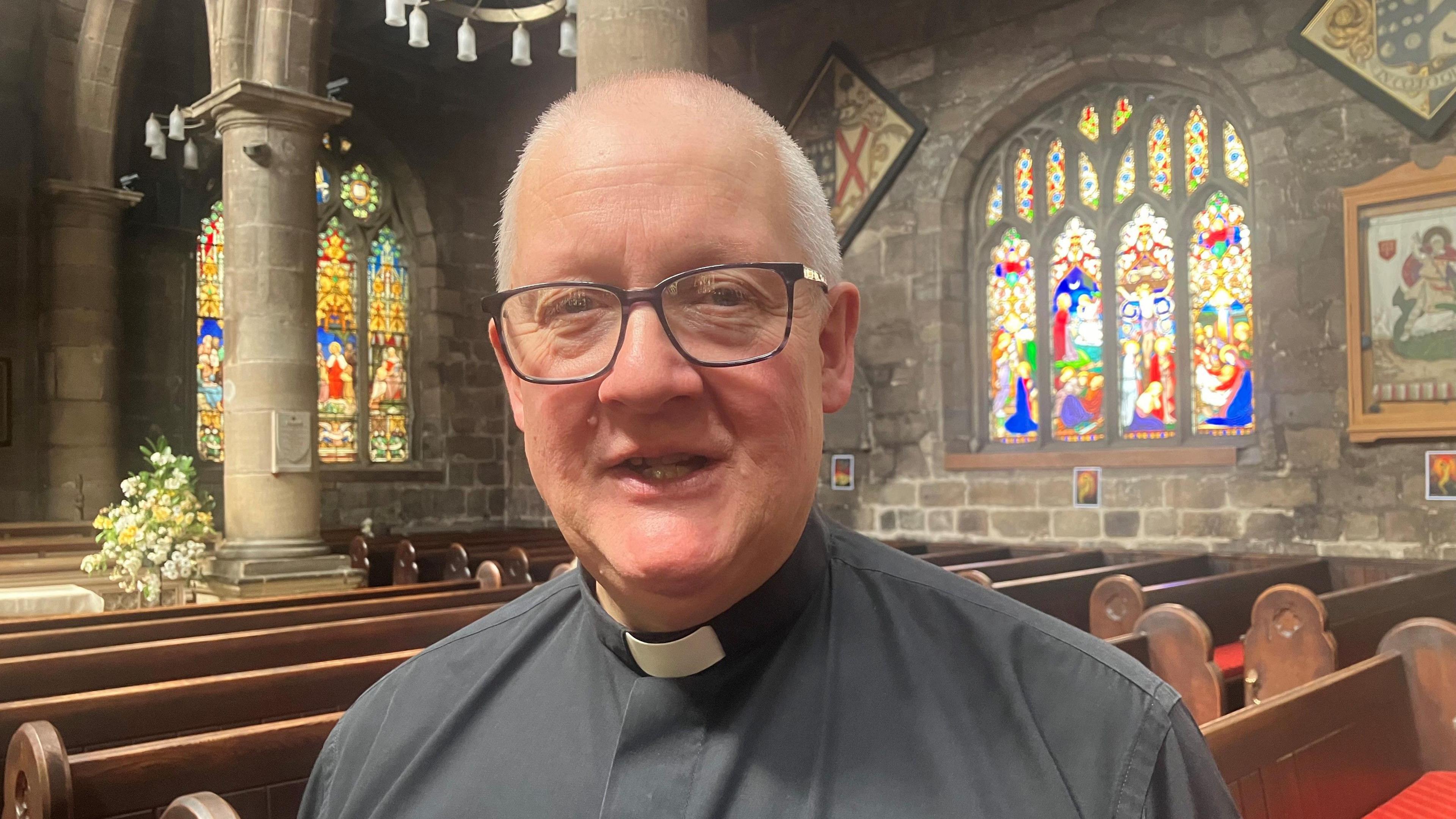 Photograph of Andrew Holliday in the nave of St Wilfrid's Church in Standish, with stained glass windows in the background.