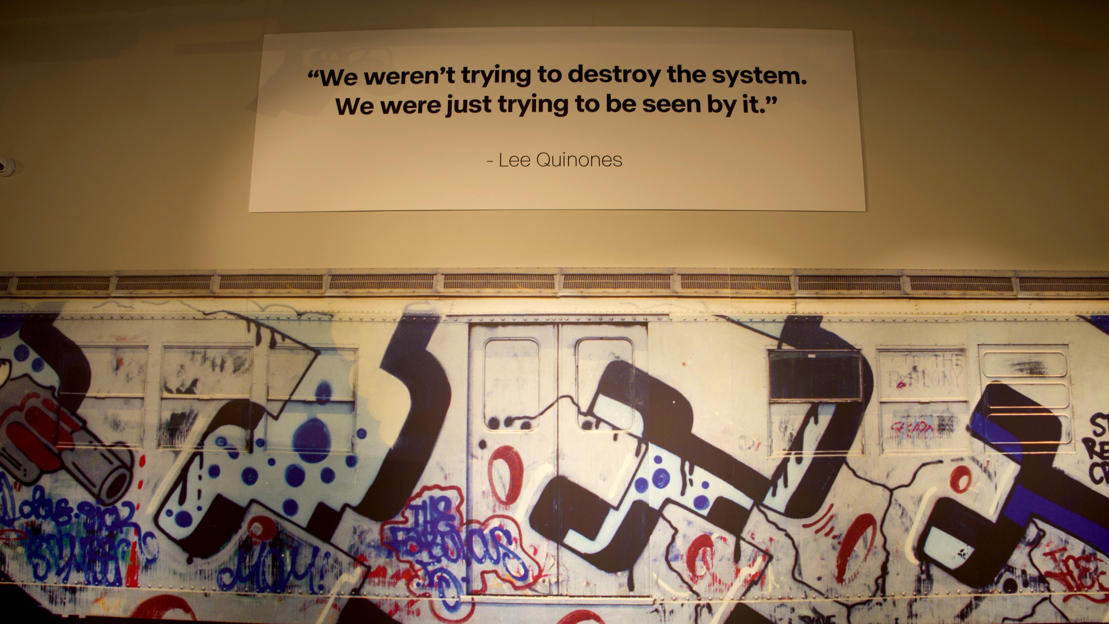 A quote above a graffitied train reads 'We weren't trying to destroy the system, we were just trying to be seen by it'.