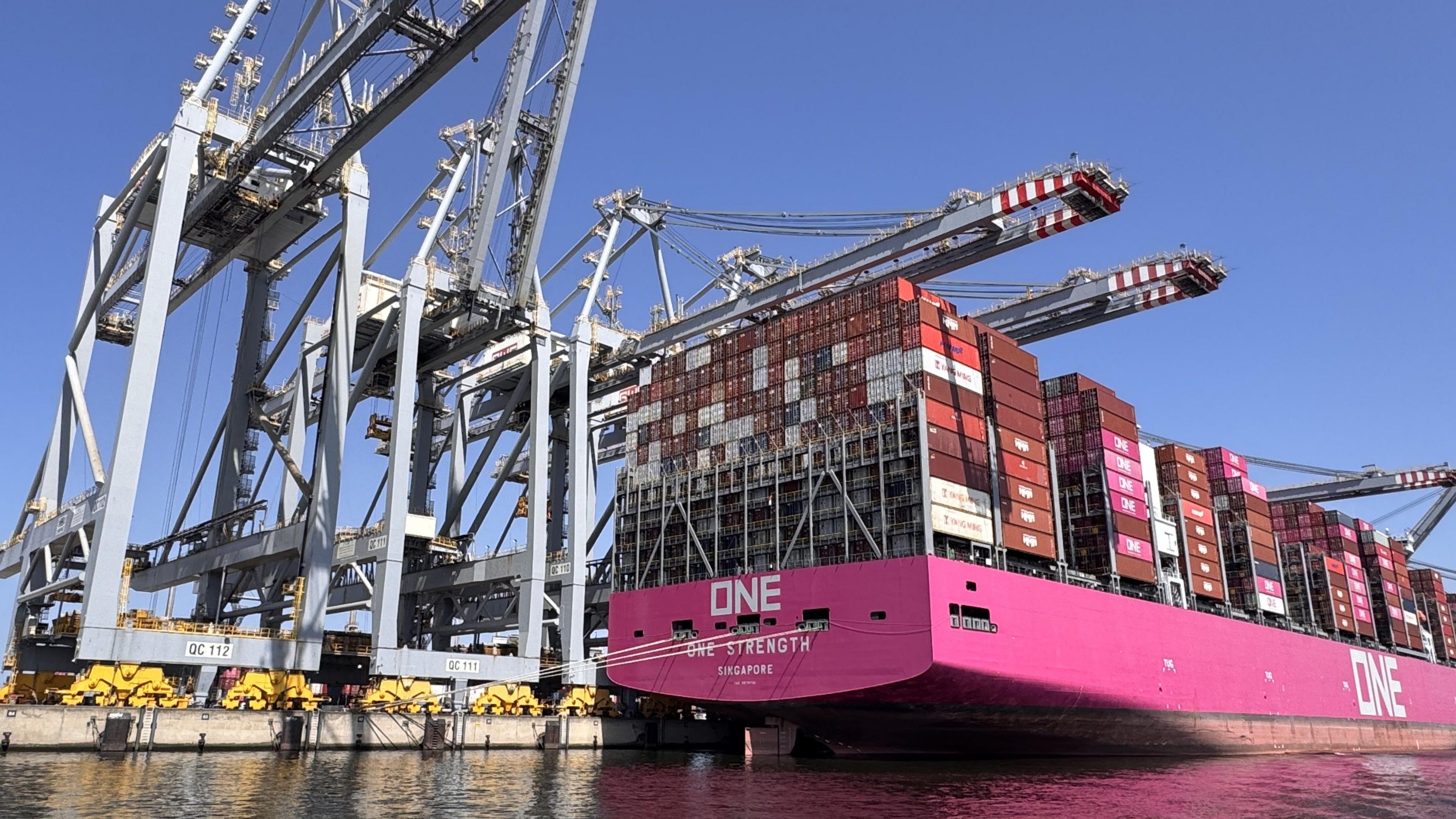A container ship with a bright pink hull is unloaded at the Port of Rotterdam