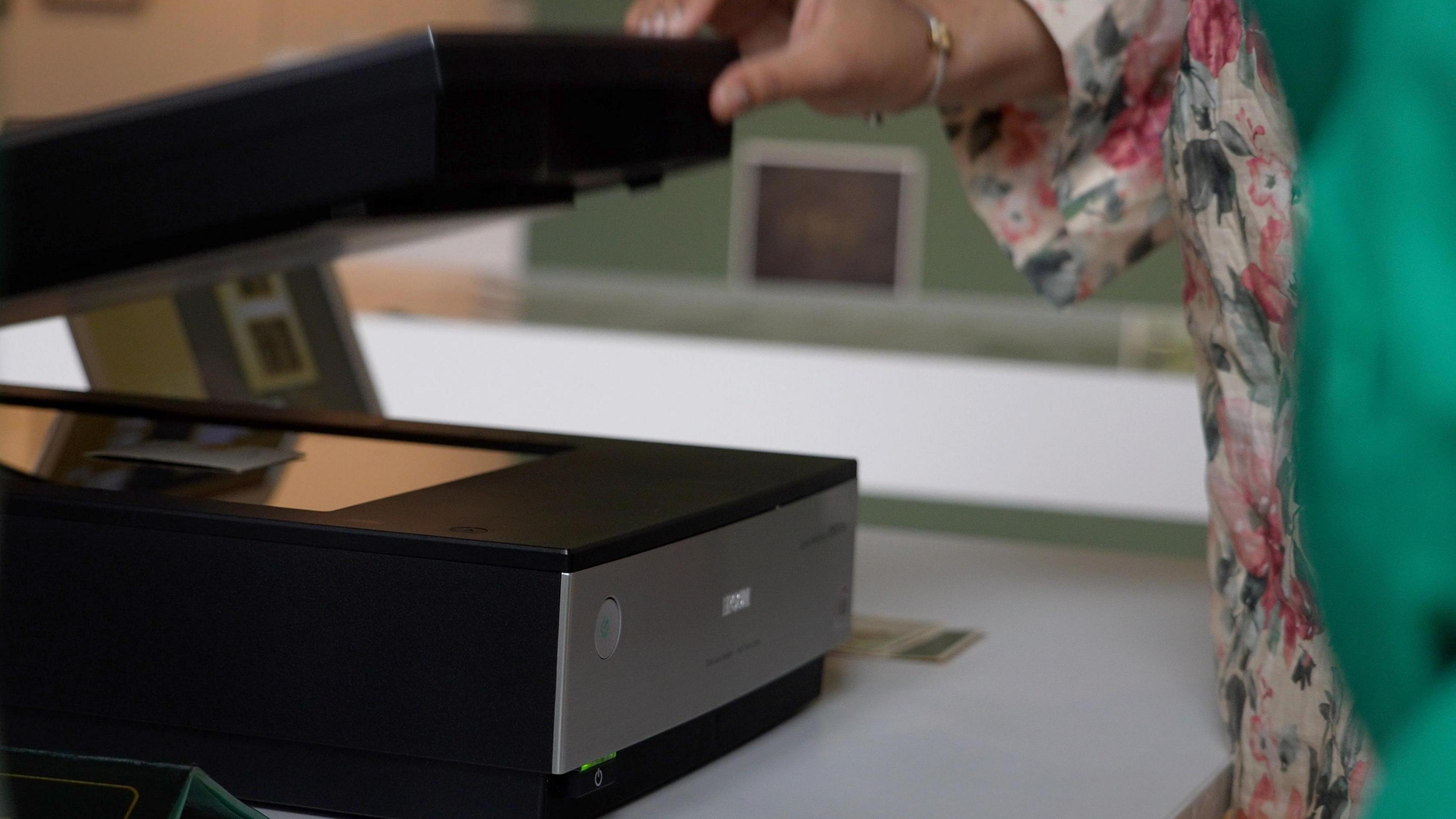 A person uses a black and silver scanner to scan photos