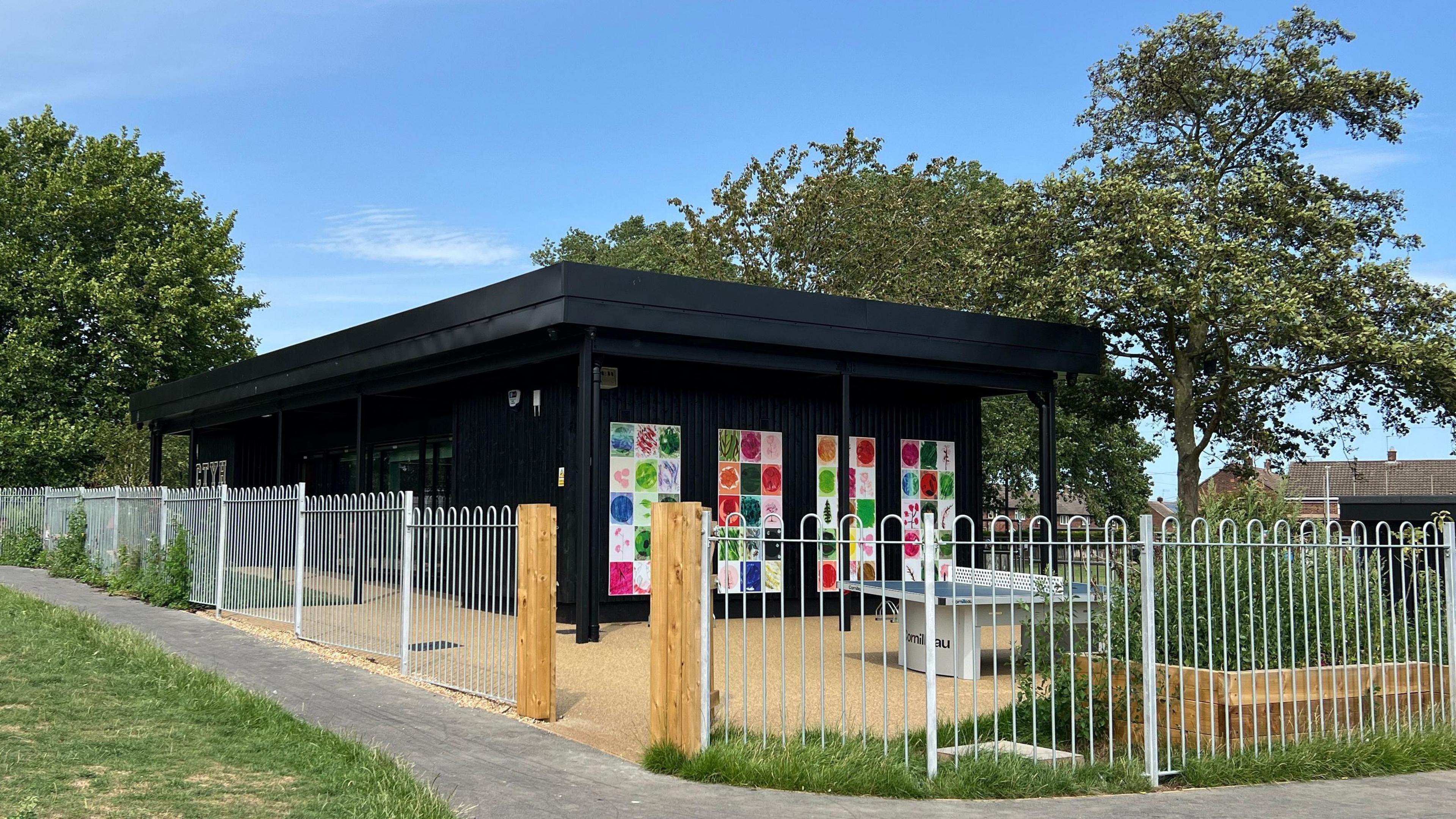 Cherry Tree Youth Hub is a black timber clad, single storey building, with art on the external walls and fenced in gardens