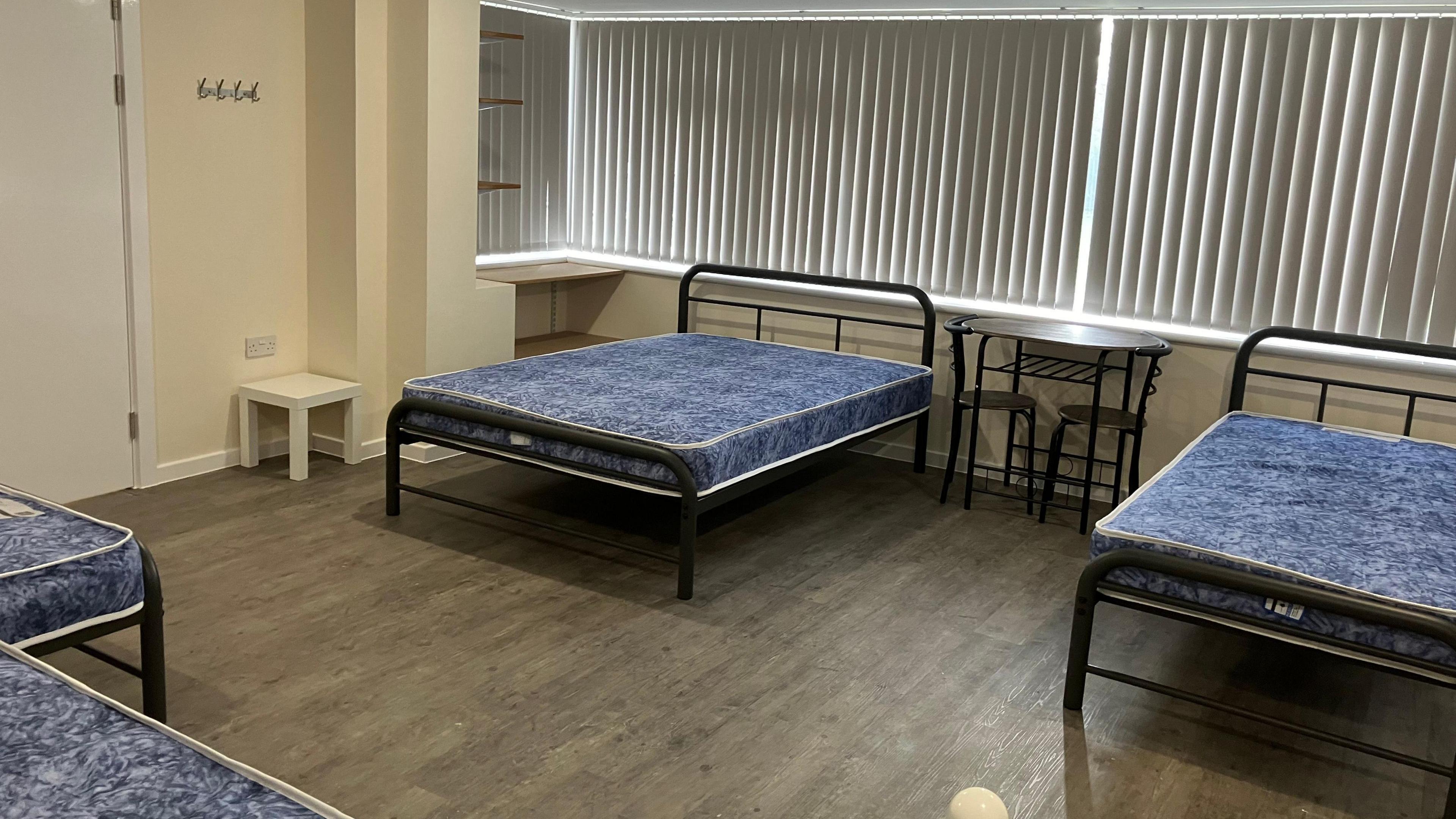 four single beds pictured, with a blue pattern on the mattress but no sheets