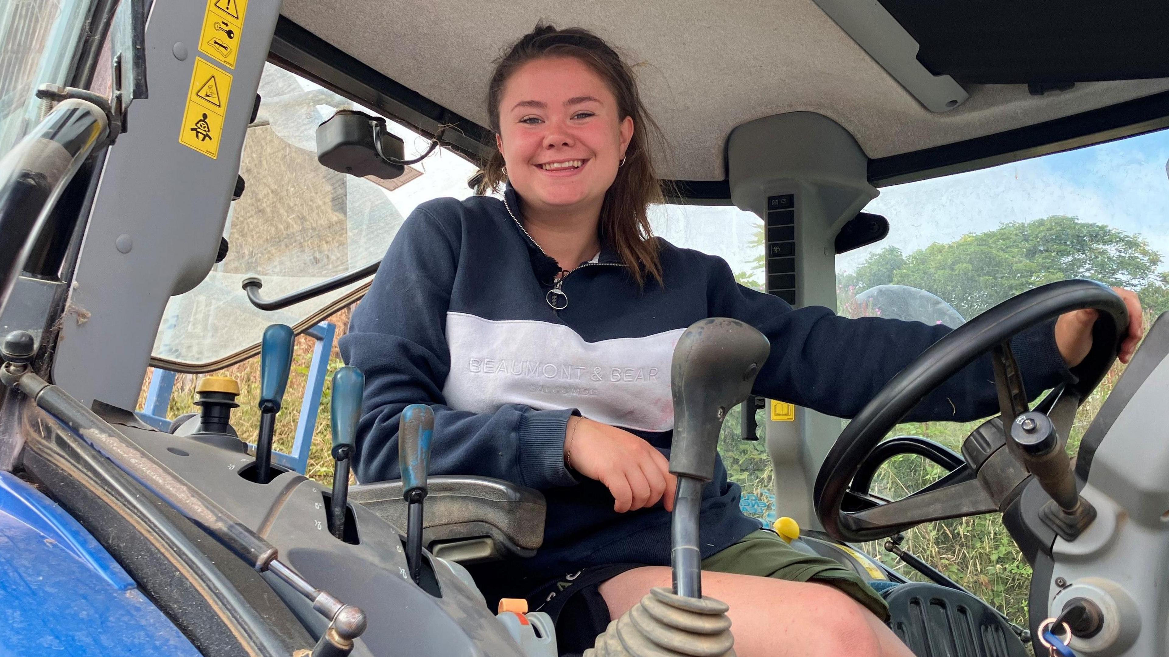 Maria Warne-Elston sitting in a tractor cab, hand on the steering wheel, smiling at the camera