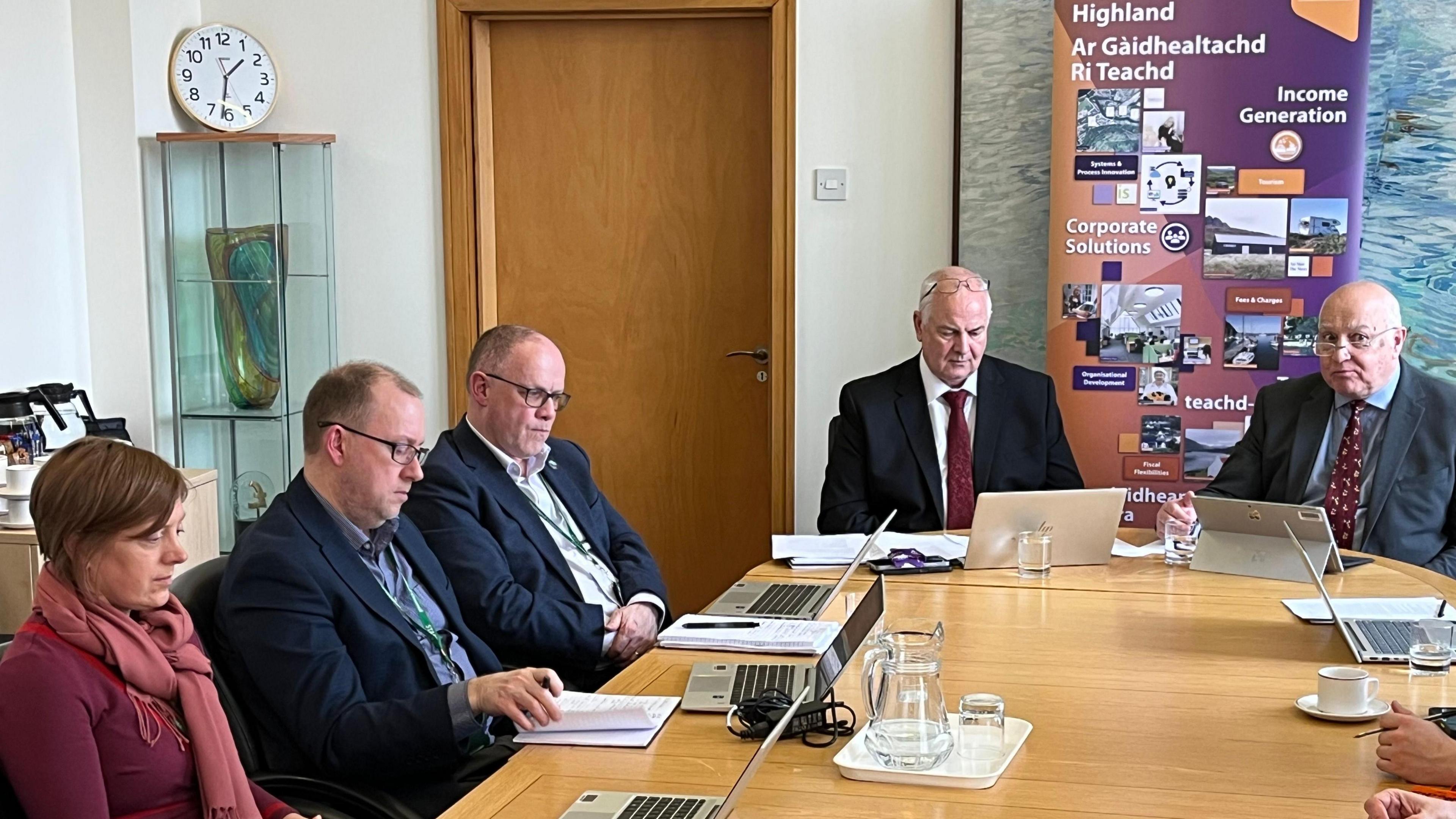 Comhairlichean na Gàidhealtachd a' suidhe aig bòrd is iad a' meòrachadh air a' bhuidseat aca.