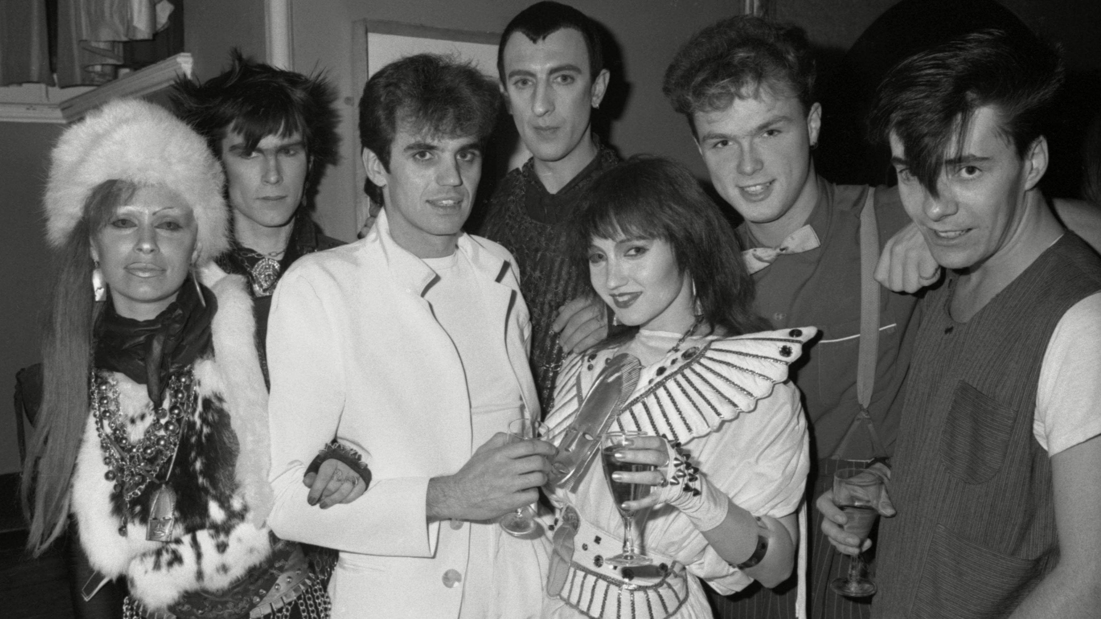 Black-and-white photo of a group of people posing at a party in 1981, including Spandau Ballet members Gary Kemp and John Keeble, performance duo Tik and Tok, and others.