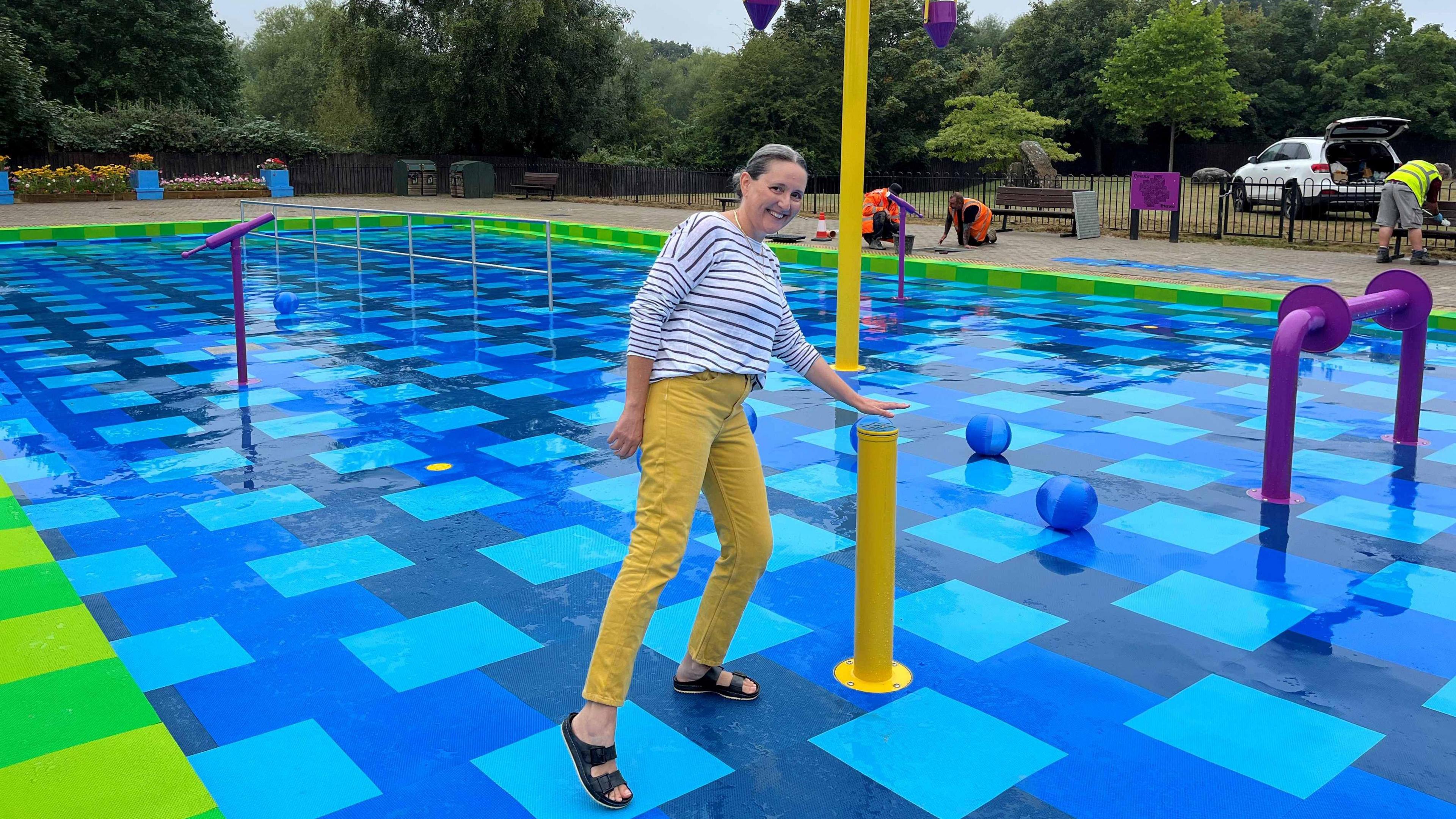 Swindon councillor Marina Strinkovsky at Coate Water Country Park. She is holding her hand above a button and smiling at the camera. 