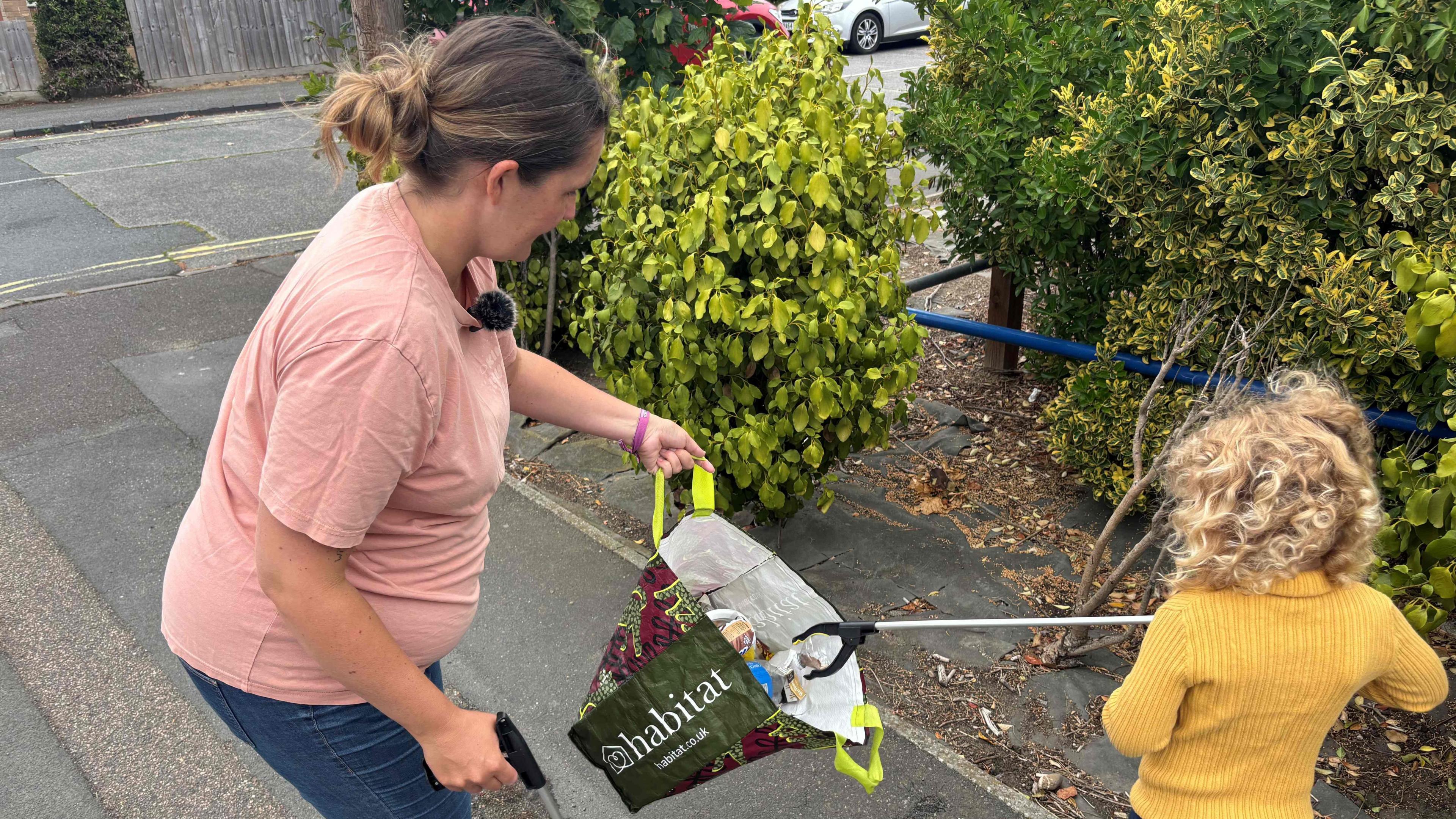 A woman and her young daughter are litter picking next to some bushes