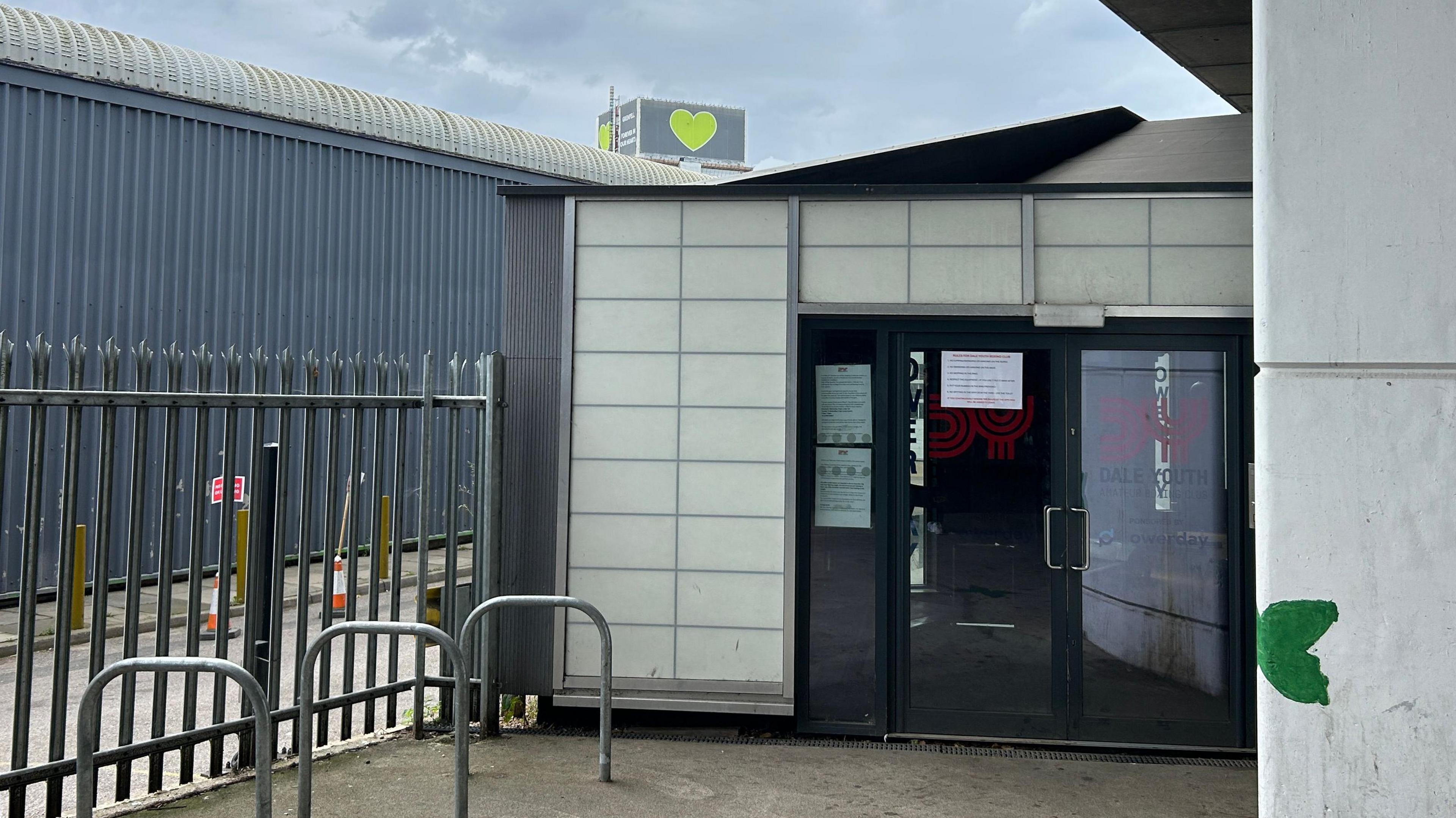 The entrance to Dale Youth Academy with a green heart at the top of Grenfell Tower in the background. 