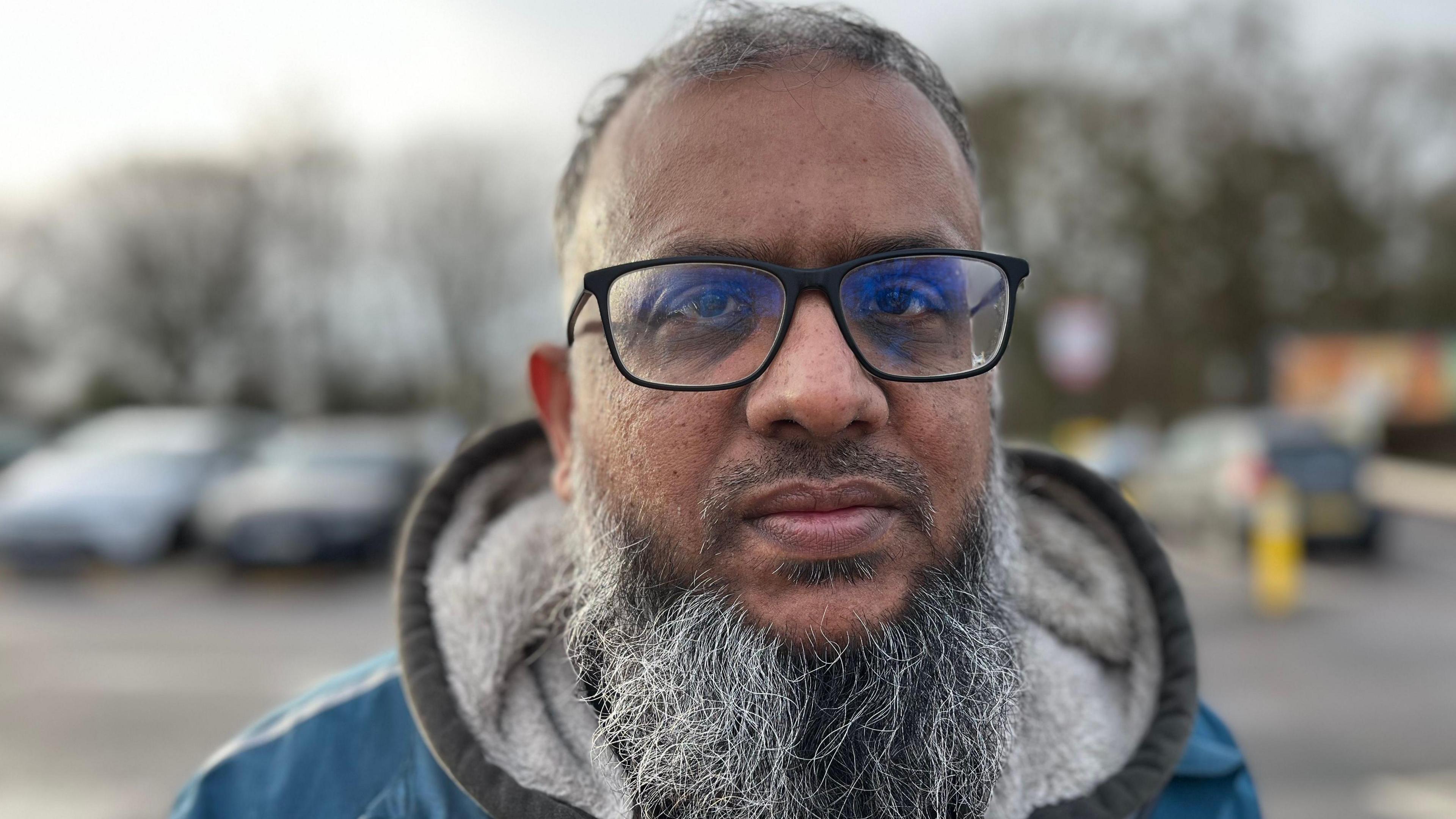 Farhan Khan wearing a jacket and glasses in a car park