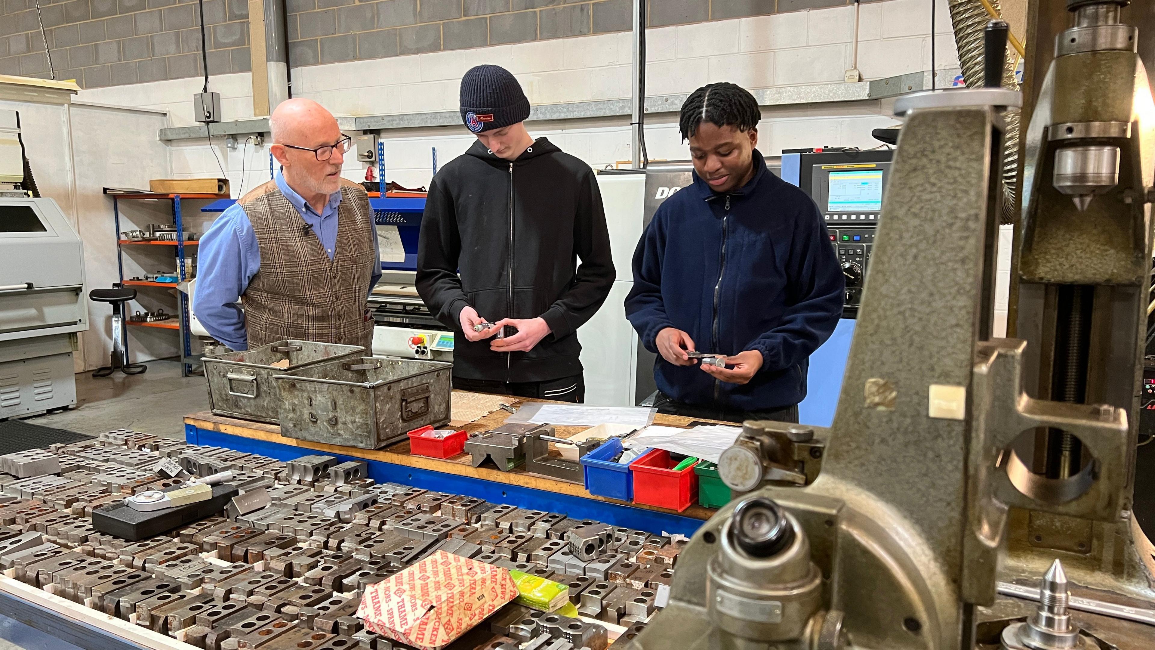 Beard and Fitch managing director Adrian Archer talking to his two apprentices who are holding to small metal gears they are producing at the factory.