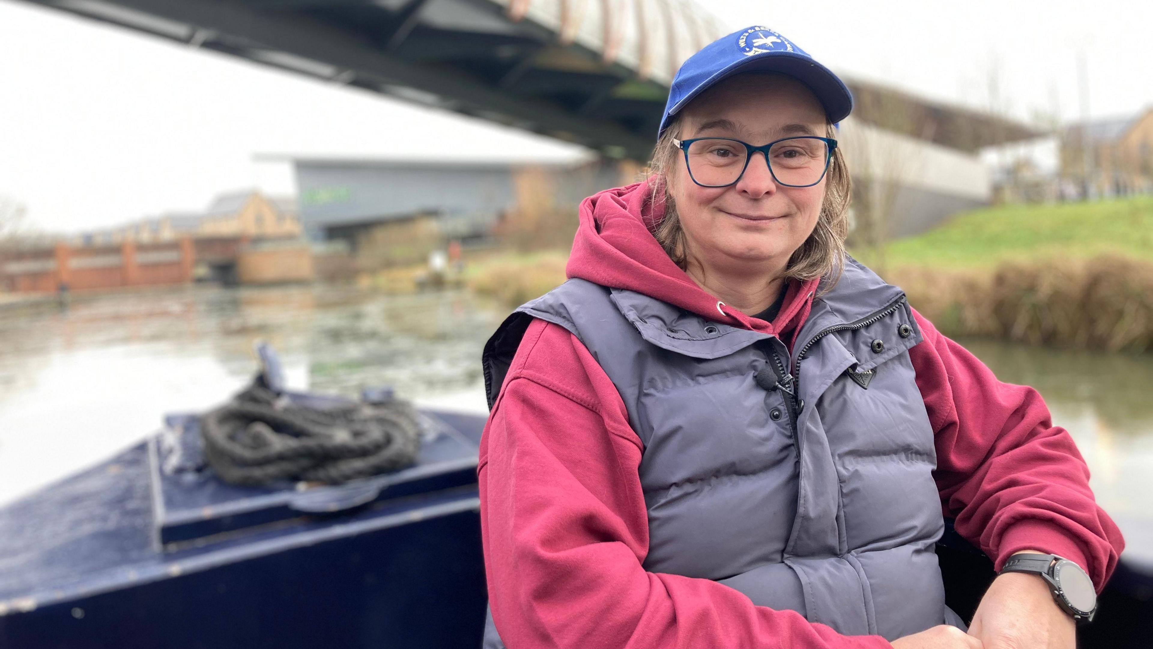 Chloe Ford is sitting on a barge that is going down a canal. She is wearing a hat and glasses.