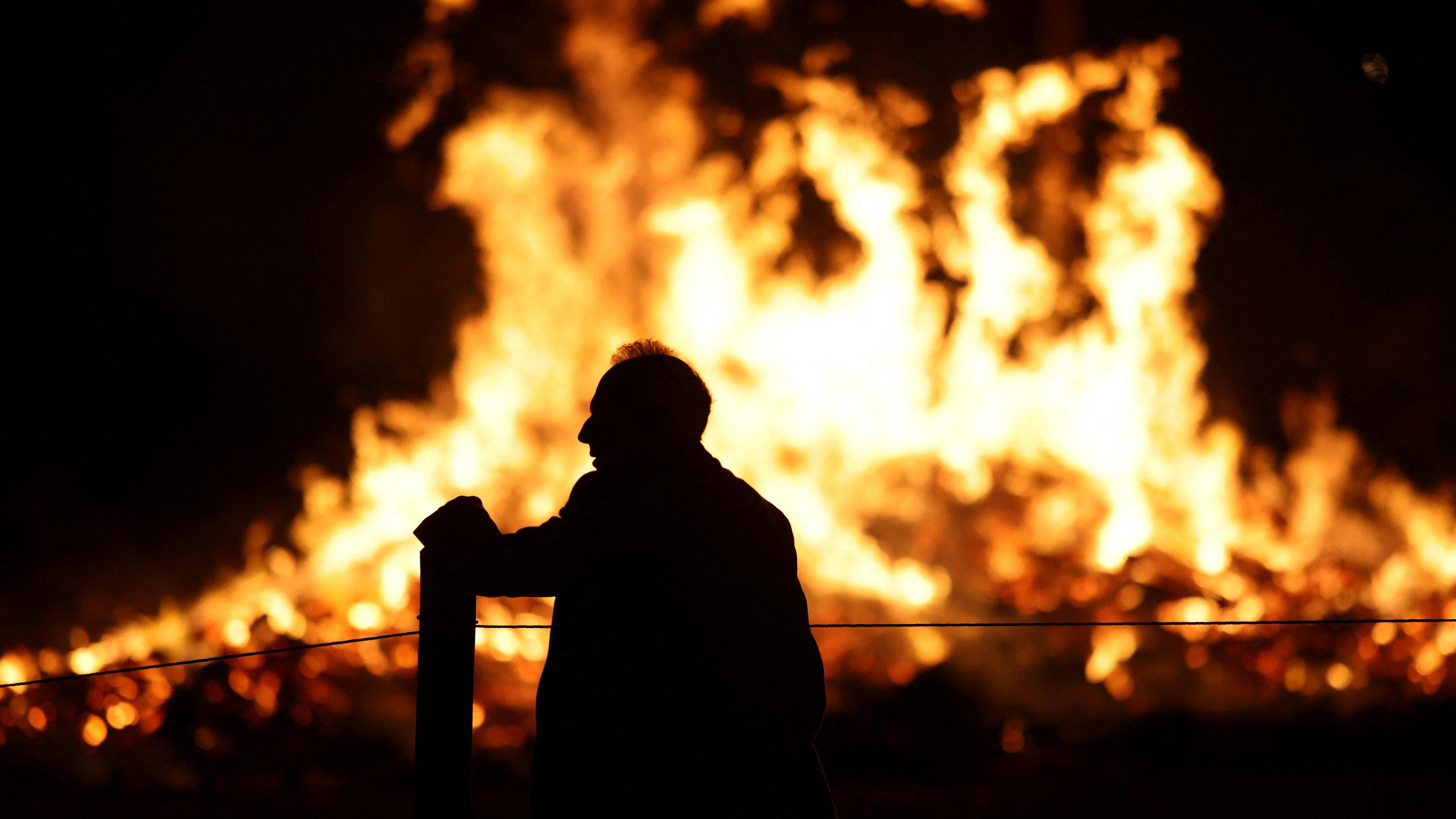 A silhouette of a man standing in front of a large bonfire