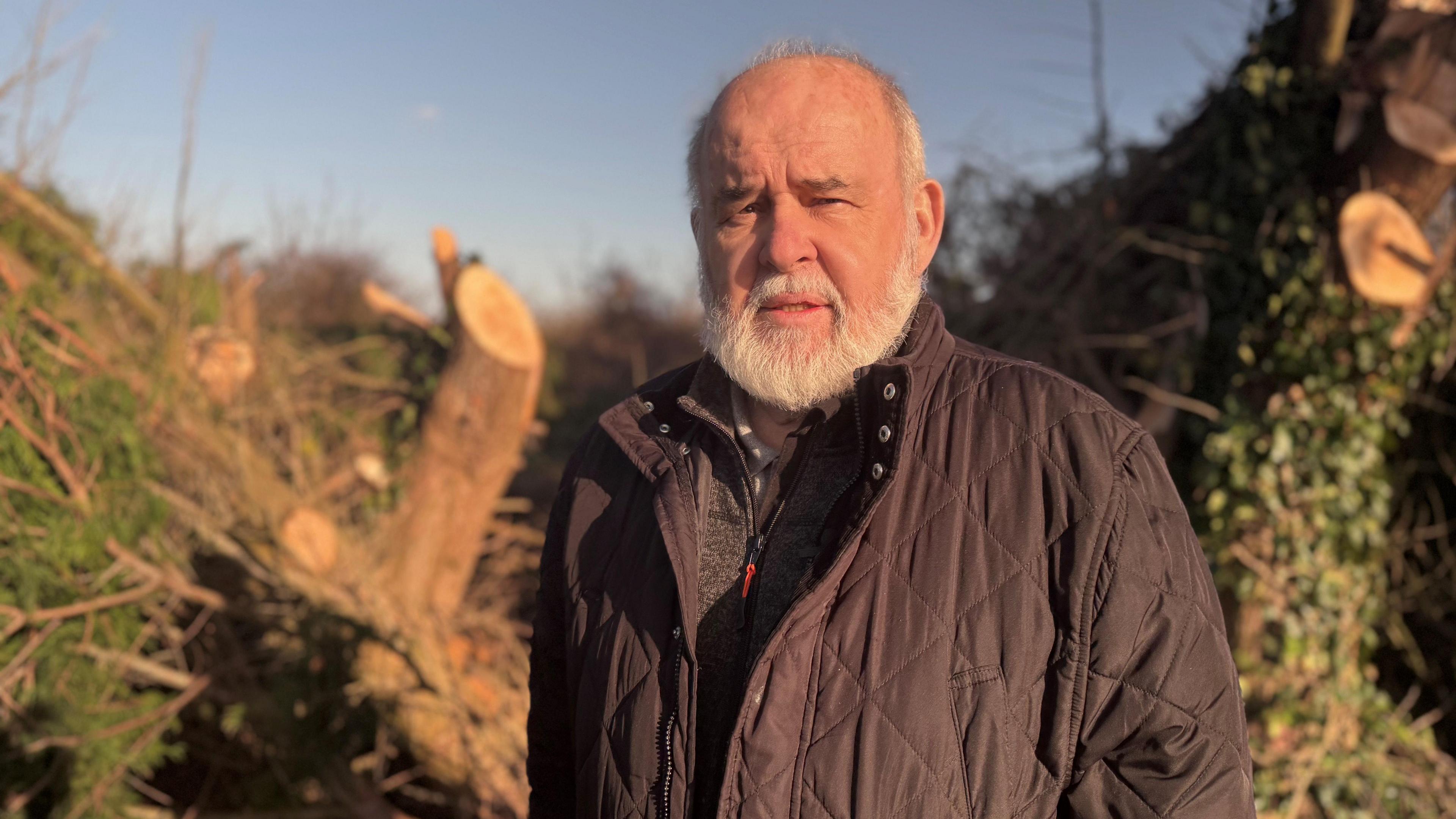 Francie Molloy has a beard. He's wearing a navy coat is is standing in front of a large uprooted tree.