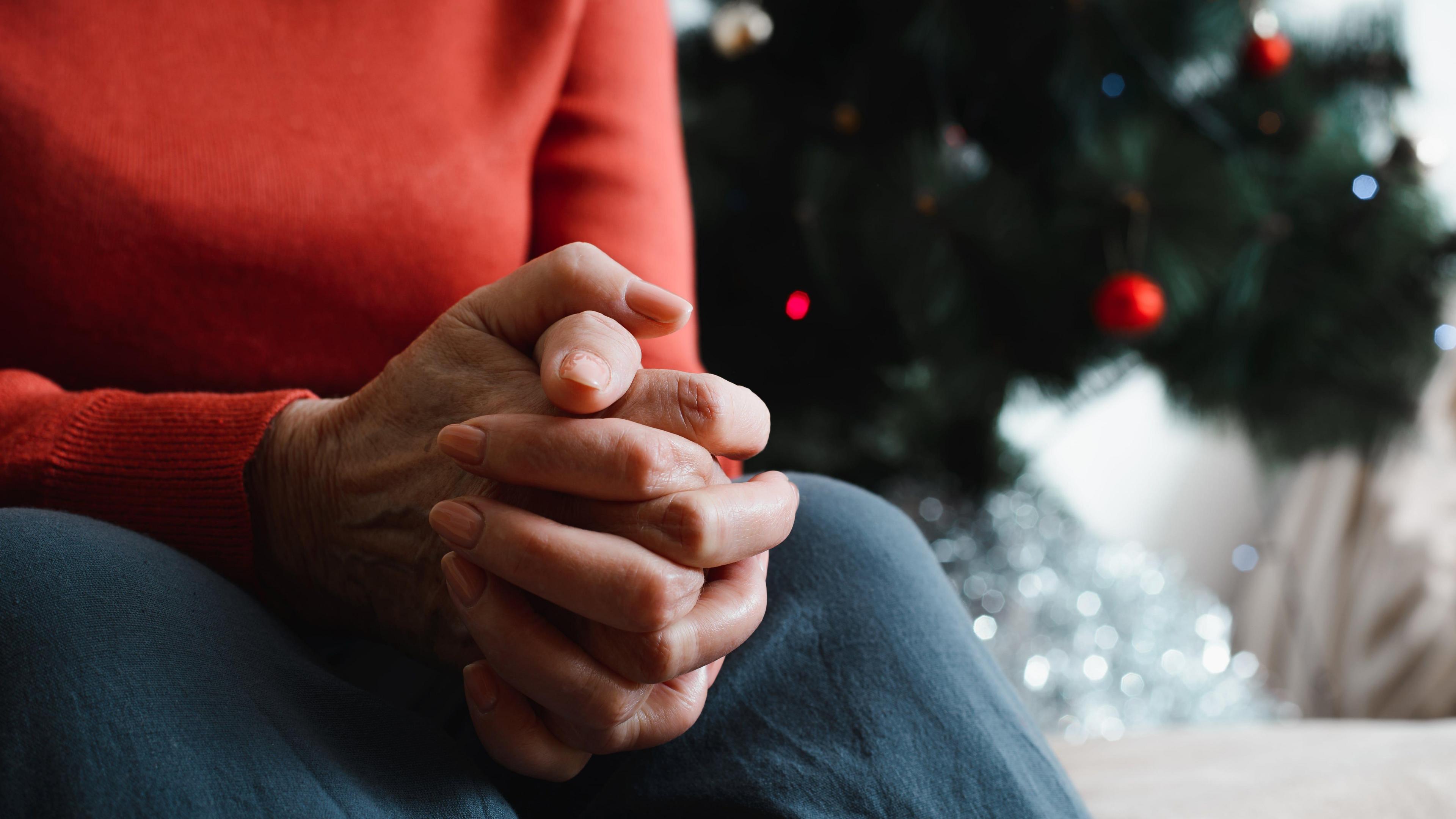 A close-up of a person with their hands together with a Christmas tree in the background.