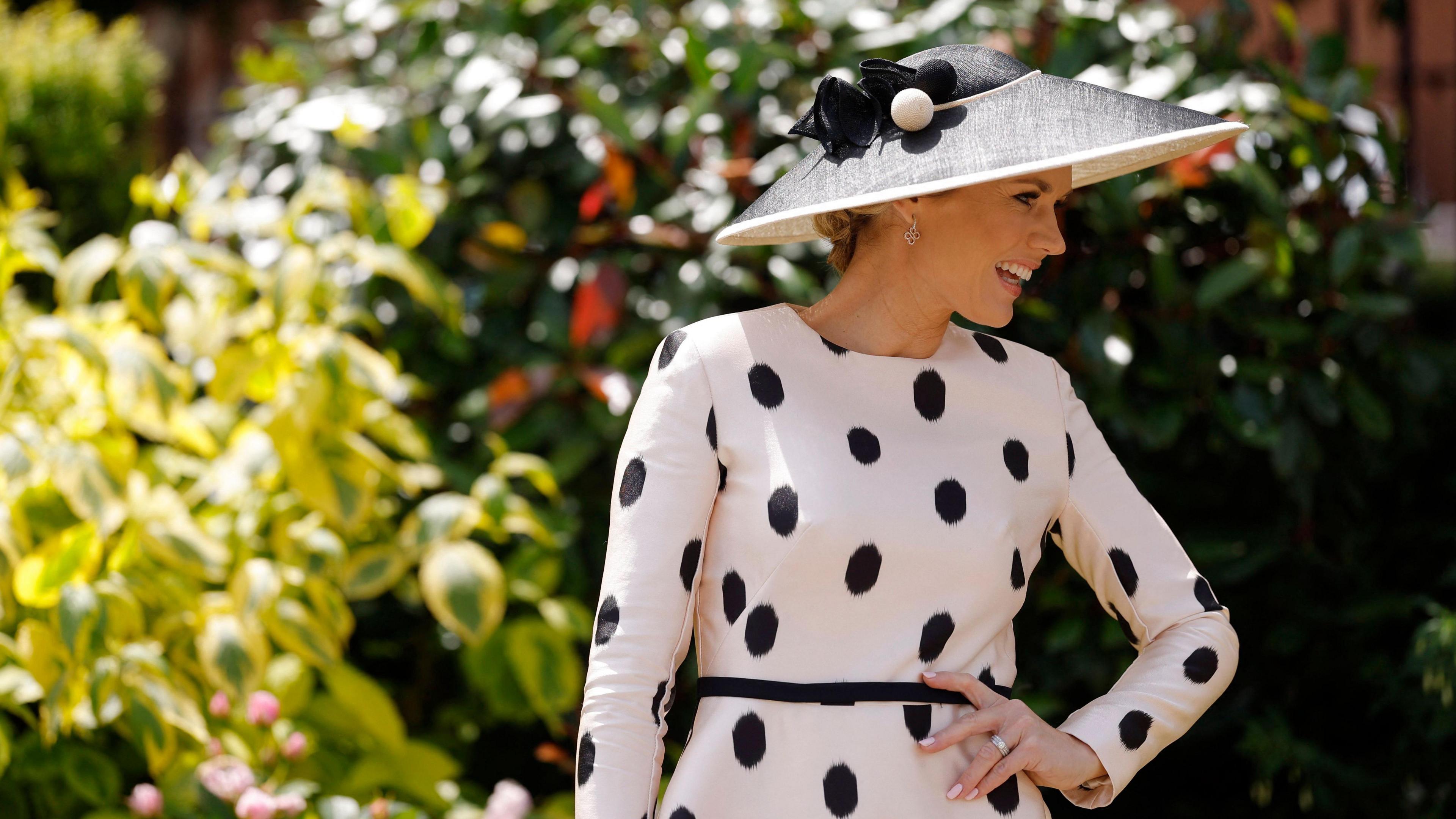 Charlotte Hawkins, a white middle aged woman poses in a white long sleeved fitted dress with black dots and a black and white hate