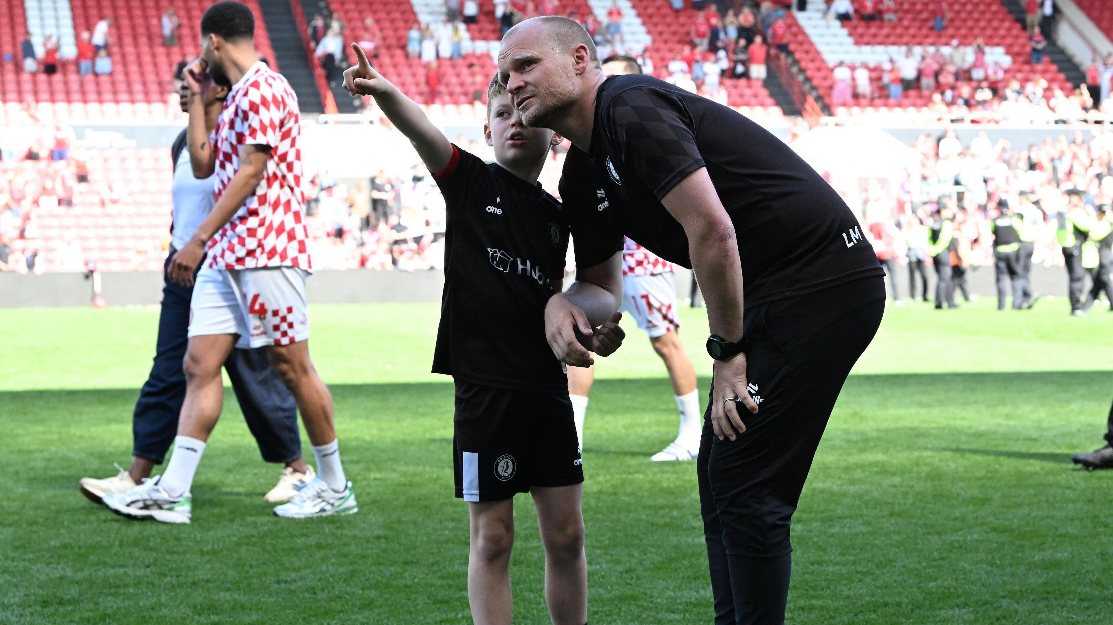 Liam Manning and his seven-year-old son, Isaac, on the Ashton Gate pitch after Bristol City confirmed their place in the Championship play-offs.