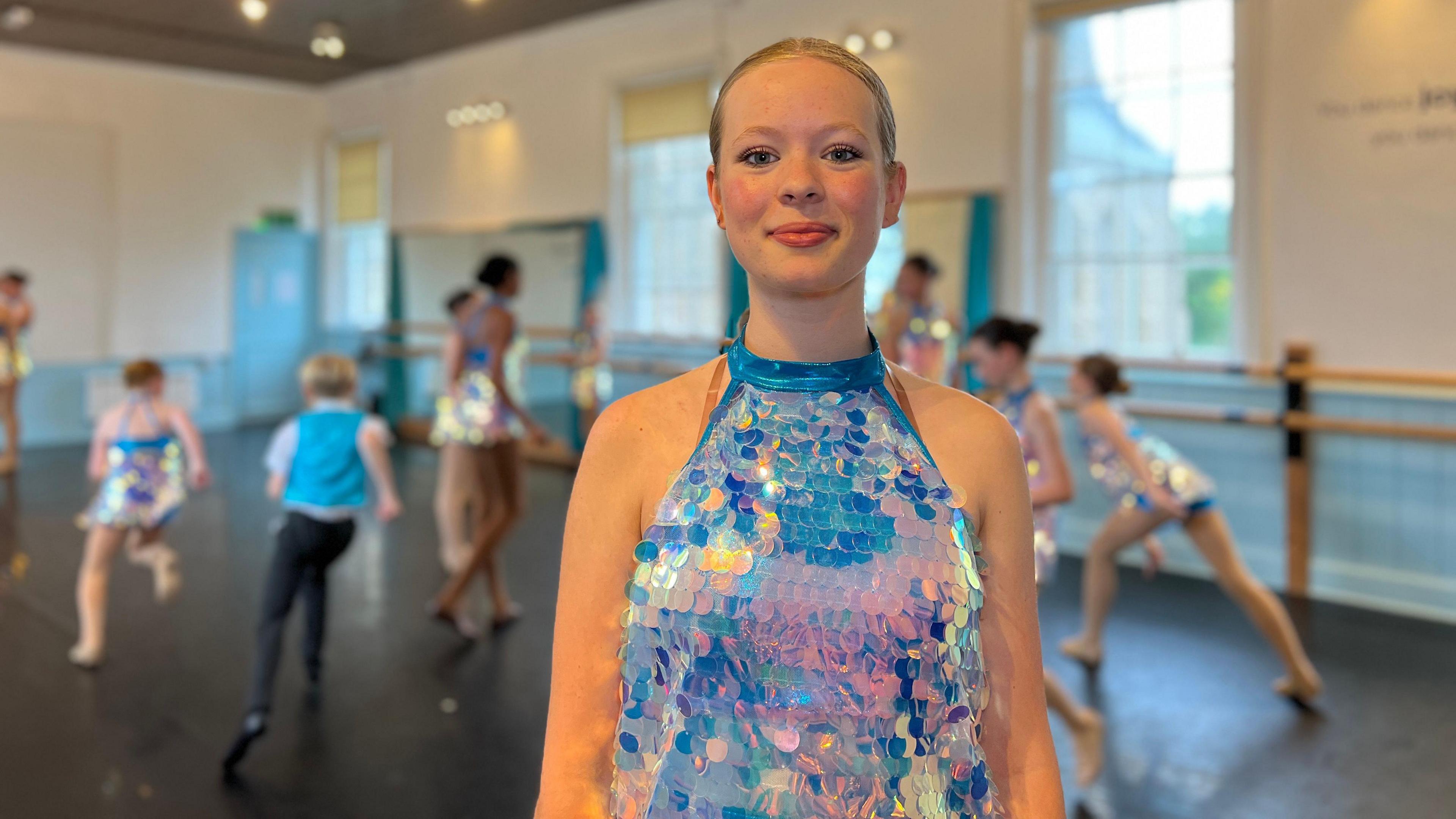 Megan smiles at the camera in a sequens dress as children dance behind her