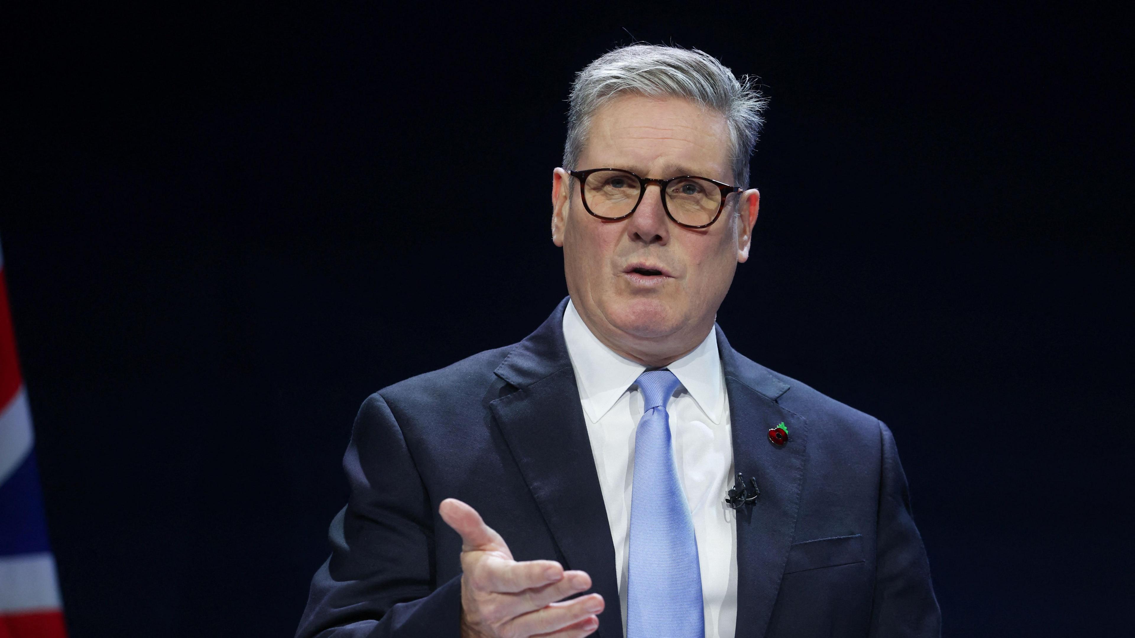 Sir Keir Starmer in a dark blue suit and blue tie with black glasses making a speech