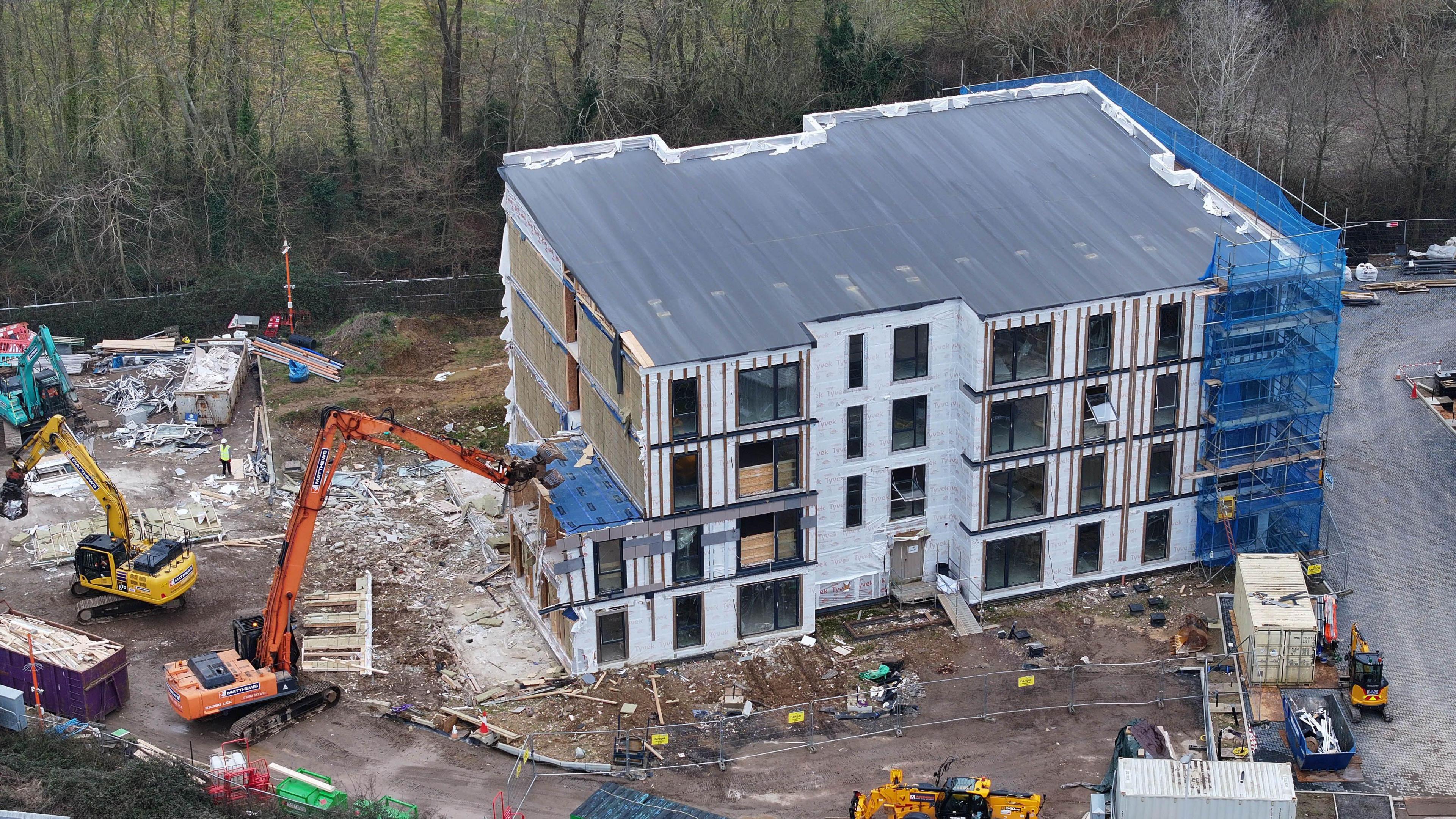 A yellow digger and an orange digger tearing down a block of new flats on a building site