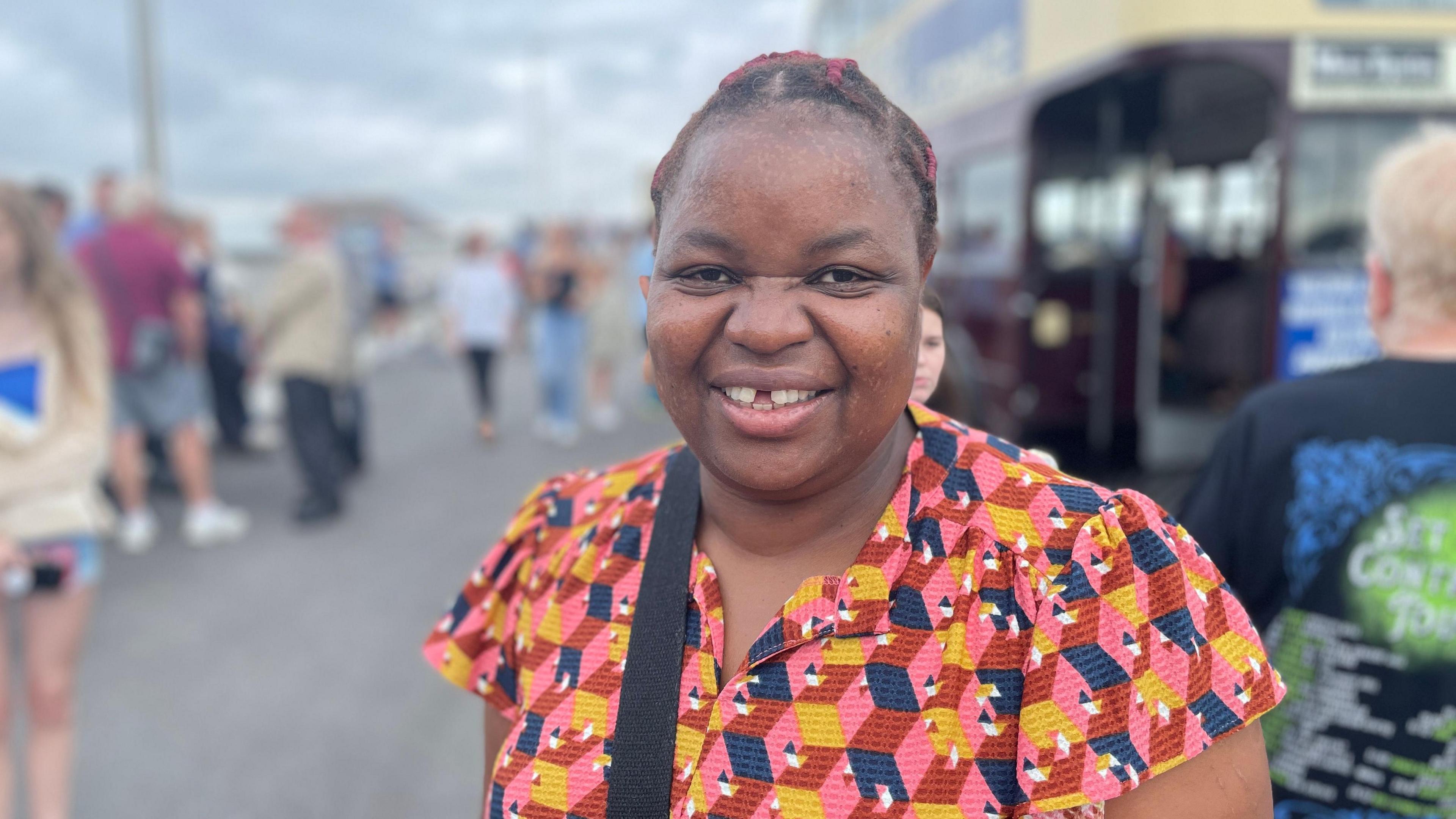 Regina Warford smiling at the camera with pedestrians and a bus out of focus in the background