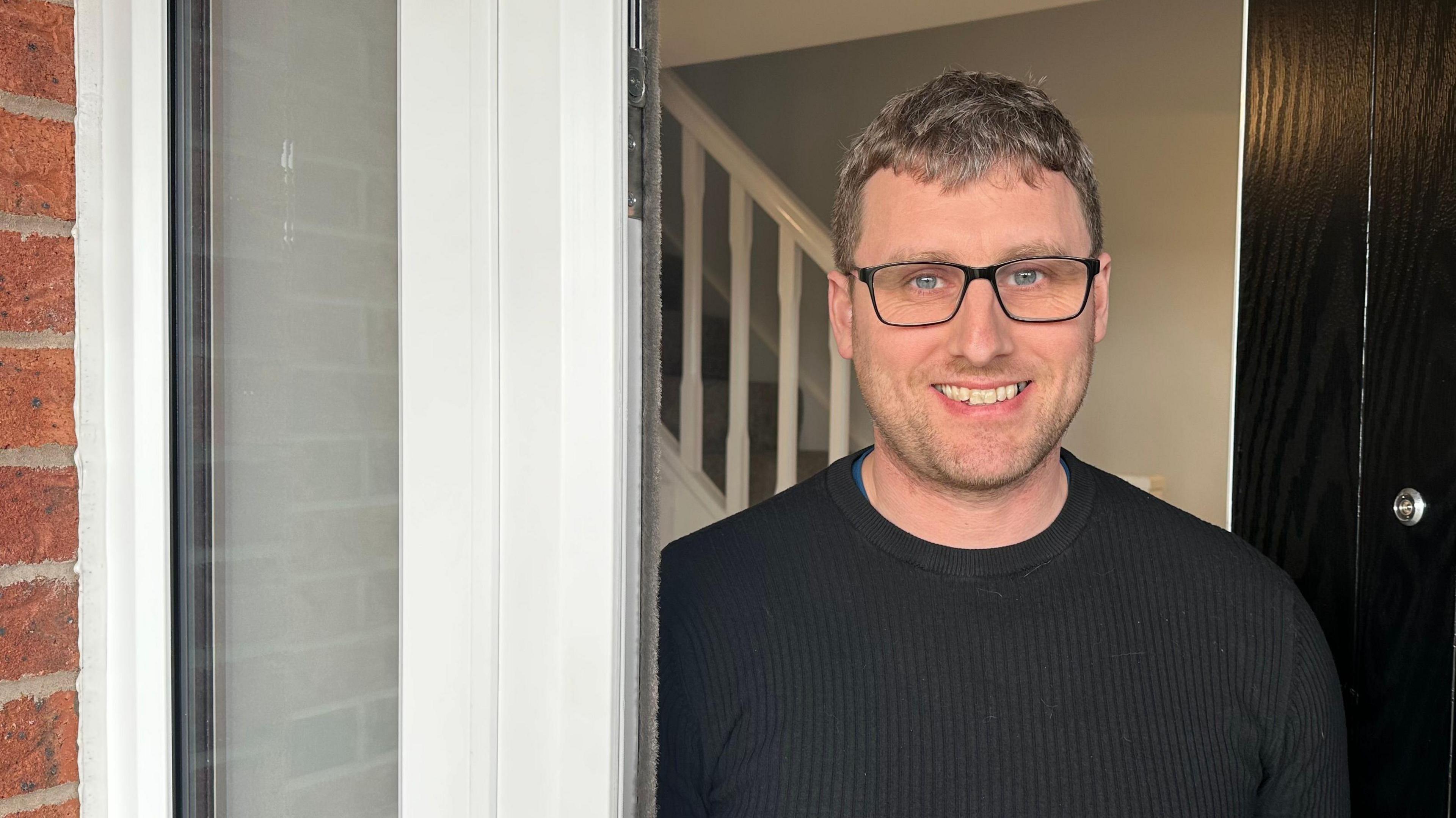 A man smiling gingerly at the open door of his house