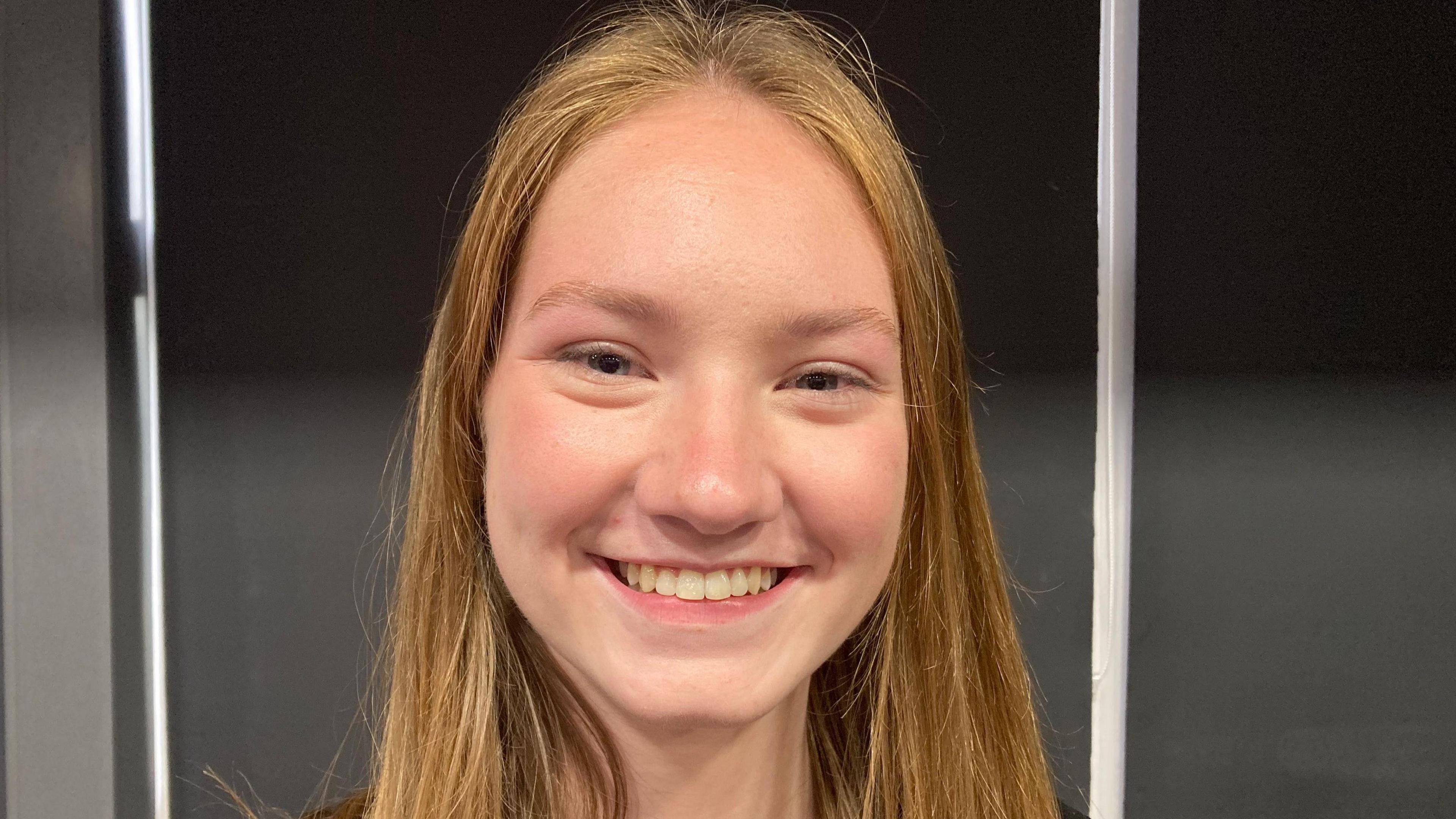 A teenage girl with long ginger hair who is smiling broadly.