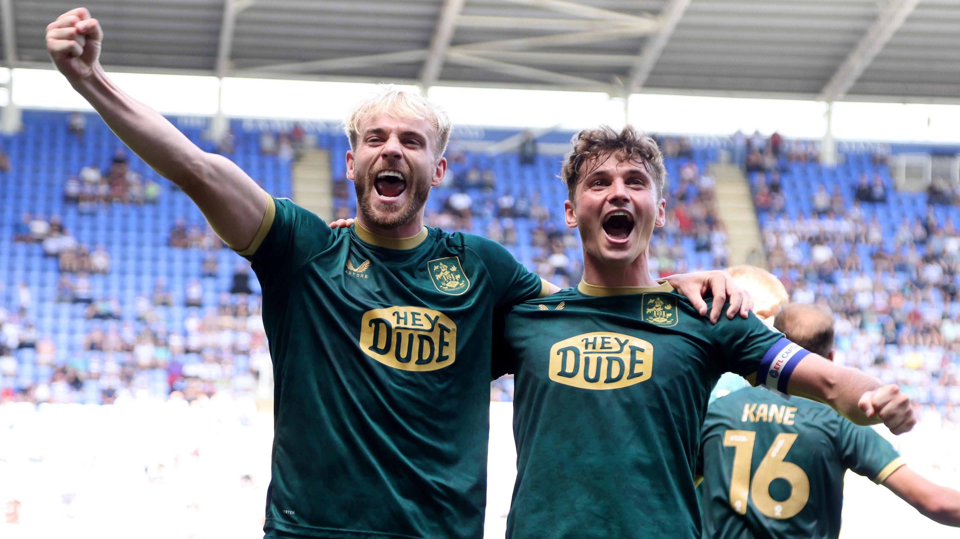 Jack Whatmough holds his right arm out high with his fist clenched and smiles with his other arm around the shoulder of team-mate Ryan Ledson in celebration