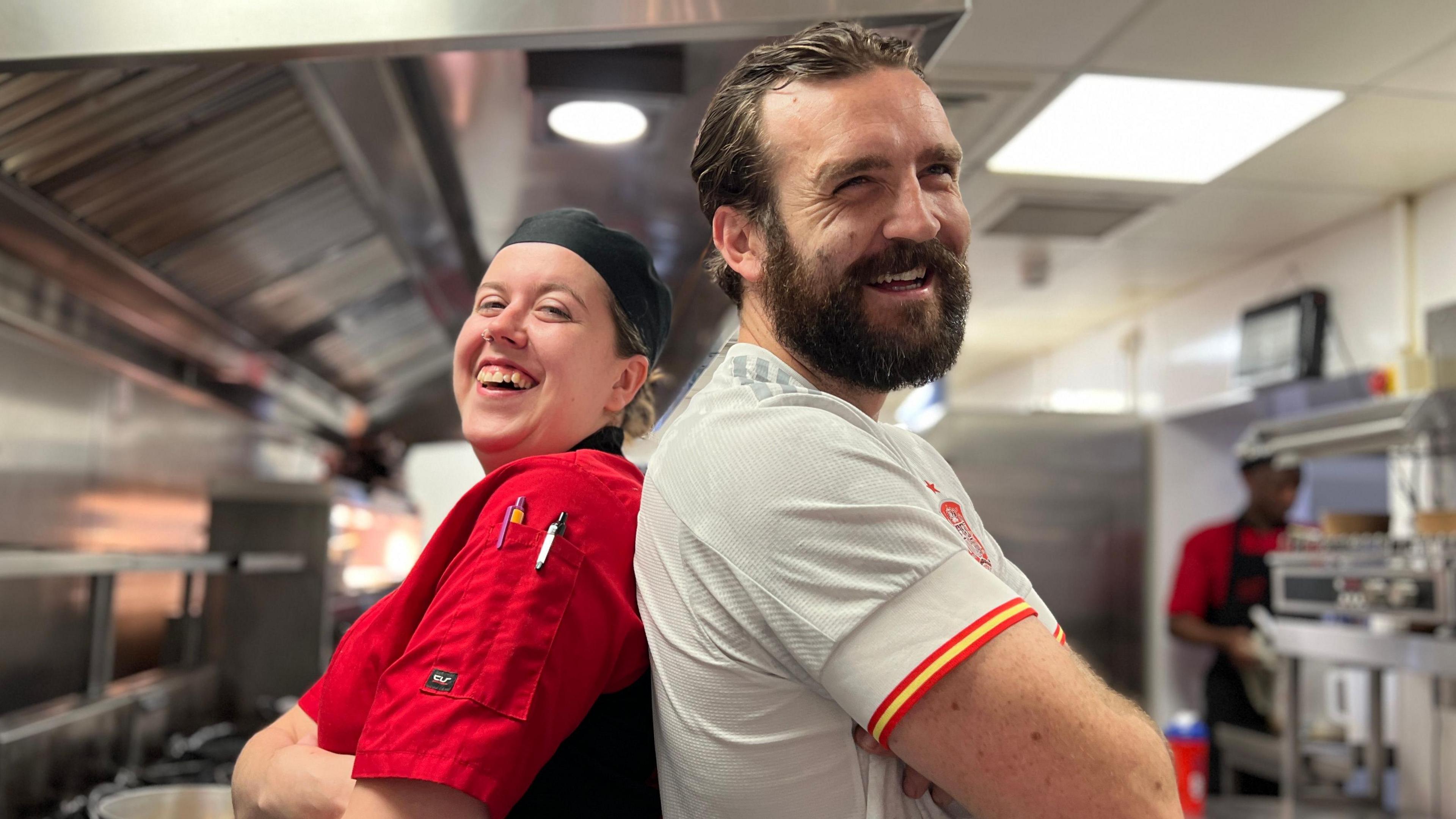 Chef Violeta Juceviciute and manager Amador Abruneiras Jr standing back-to-back and smiling in the kitchen of the Olé Olé restaurant. In the background are chrome cooking units.